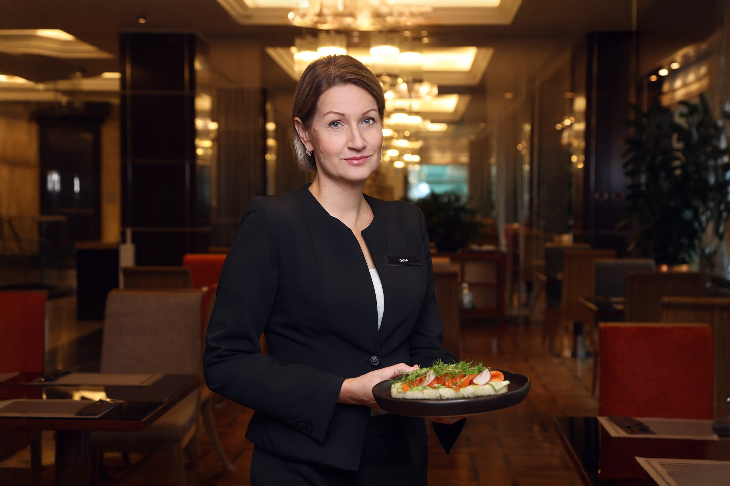 Официант ресторана отеля в классической униформе с фирменным блюдом на подносе. Дружелюбная улыбка.