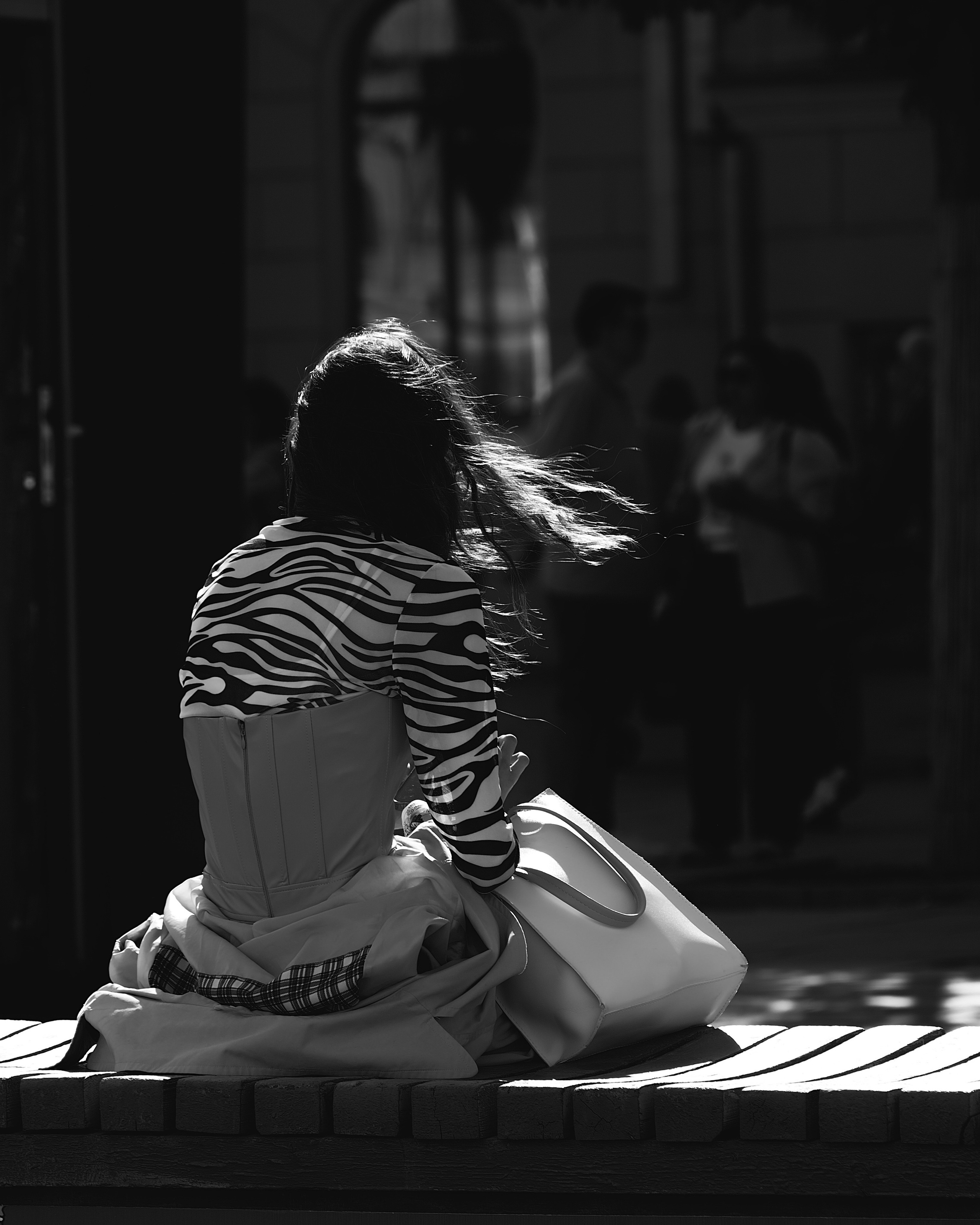 Девушка с развивающимися волосами сидит на тумбе 