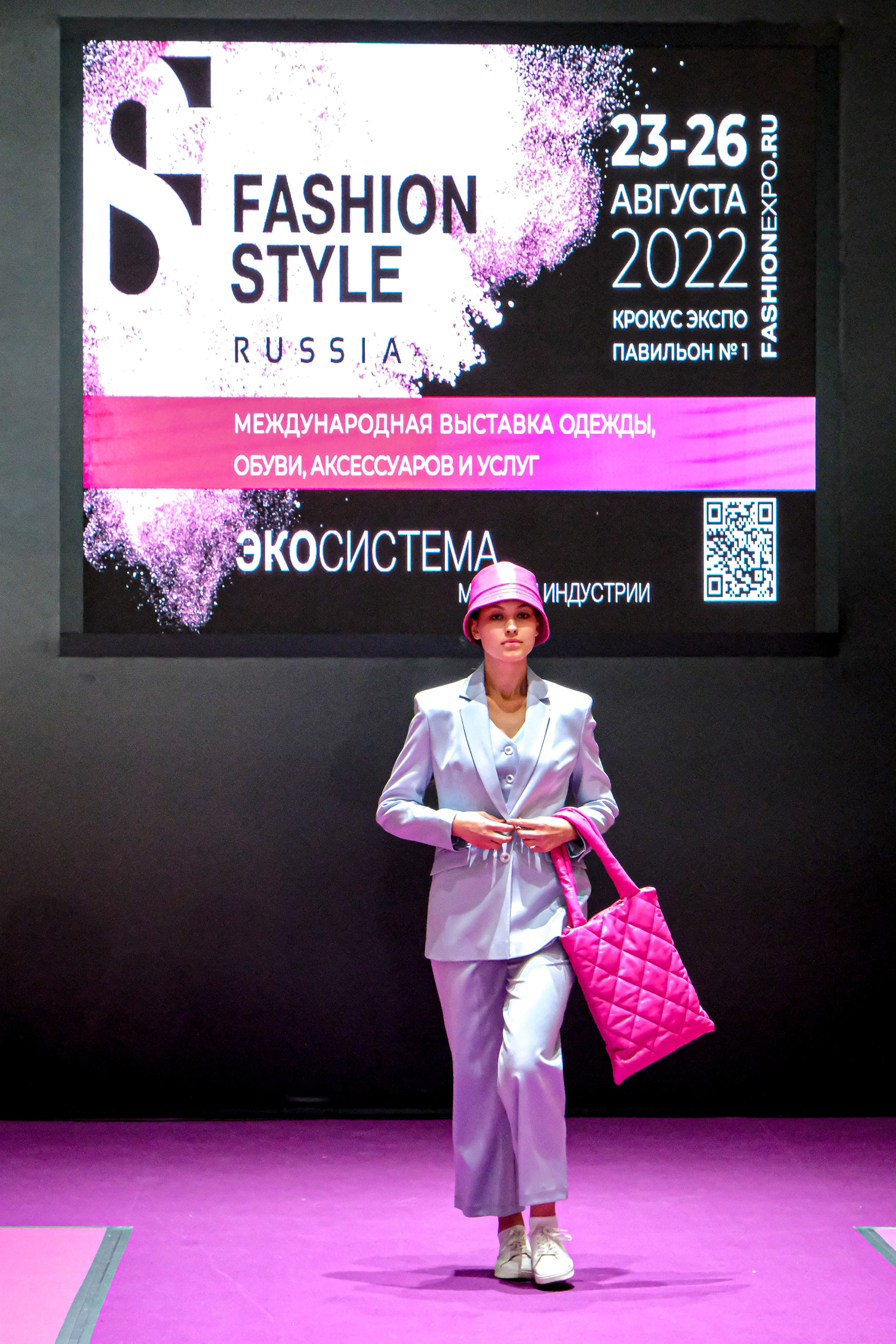  "Модели в ярких нарядах проходят по подиуму во время показа мод, освещенные яркими софитами и окруженные восторженными зрителями."