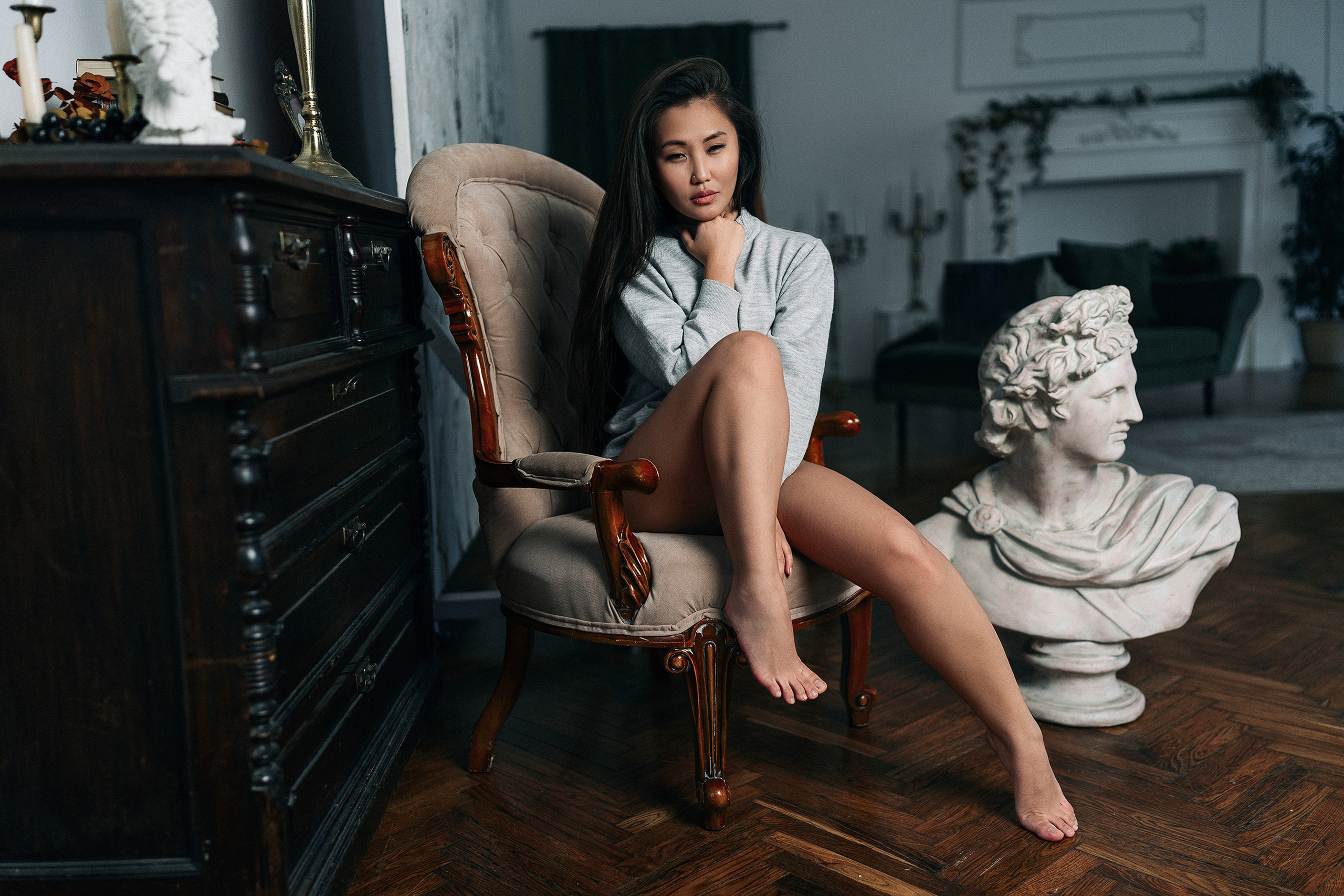 Девушка с азиатской внешностью в серой кофте и черных трусиках  сидит в кресле