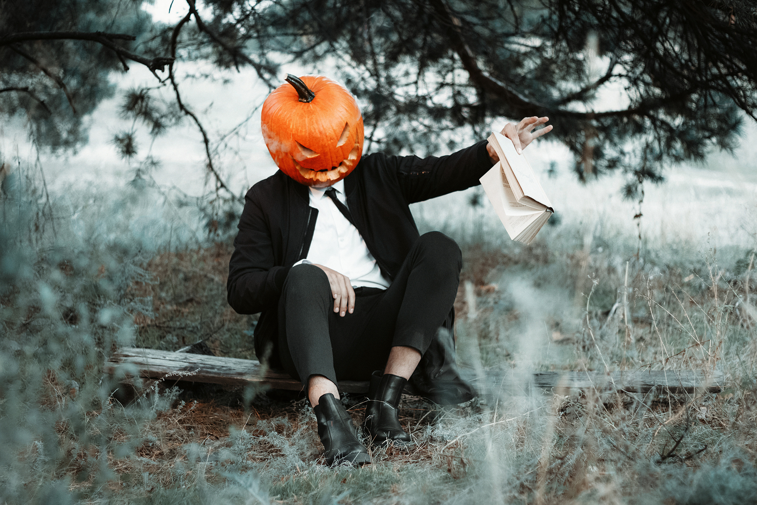 Парень в строгом костюме в маске тыквы держит за край книгу