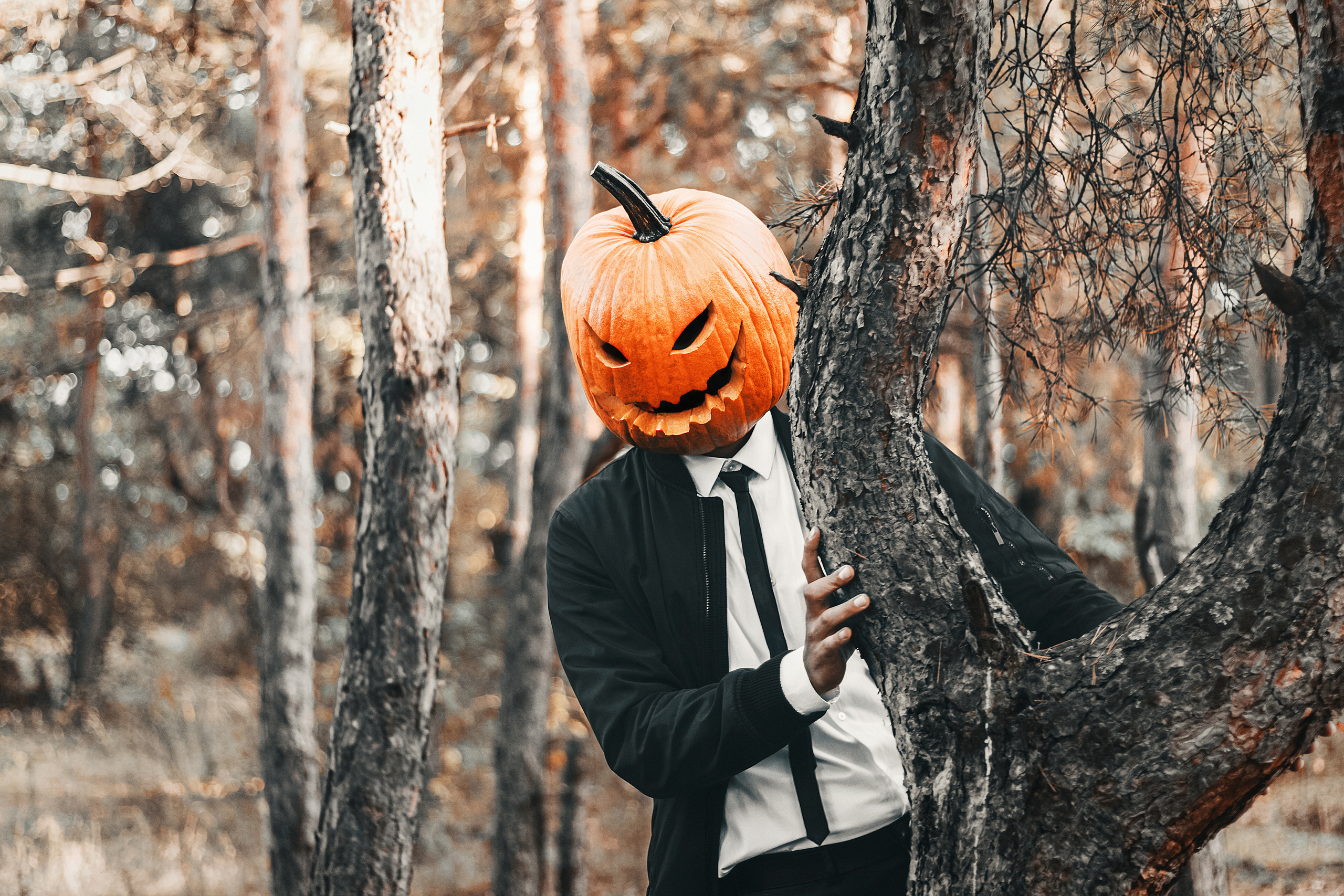 Парень в строгом костюме в маске тыквы стоит у дерева. Автор: Роман Яковенко