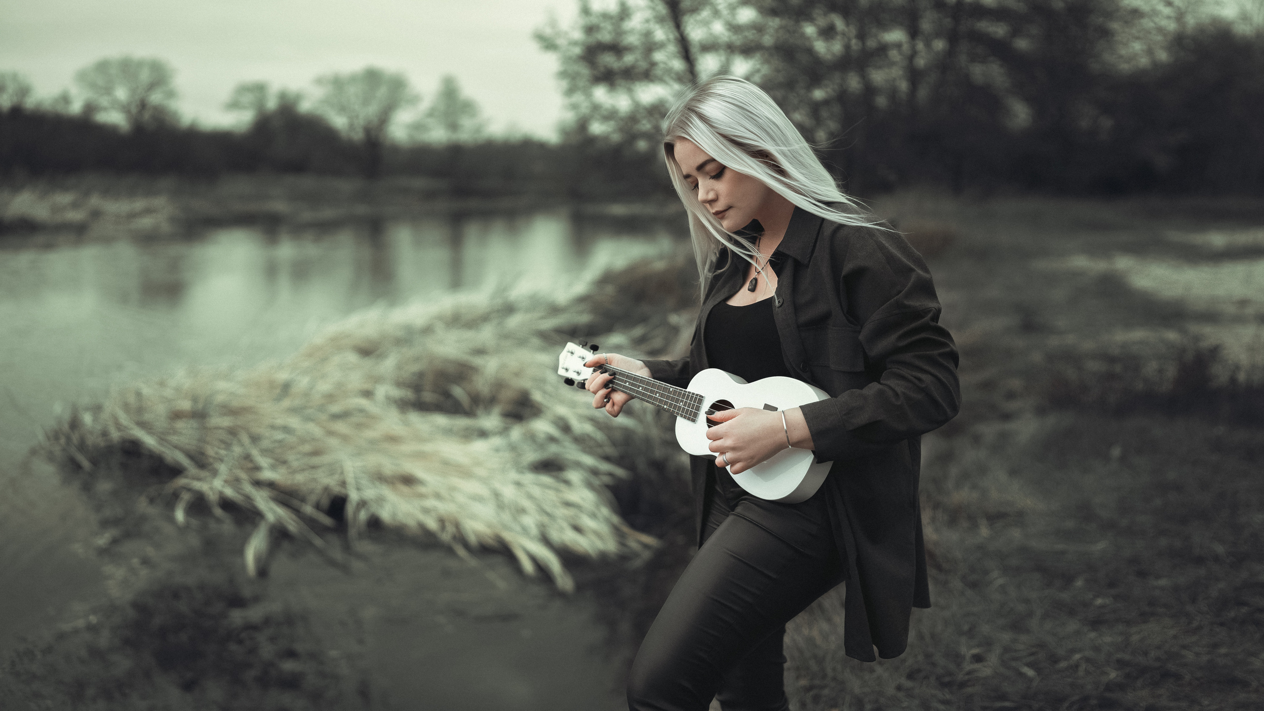 Девочка блондинка с укулеле у берега реки играет красивую музыку 