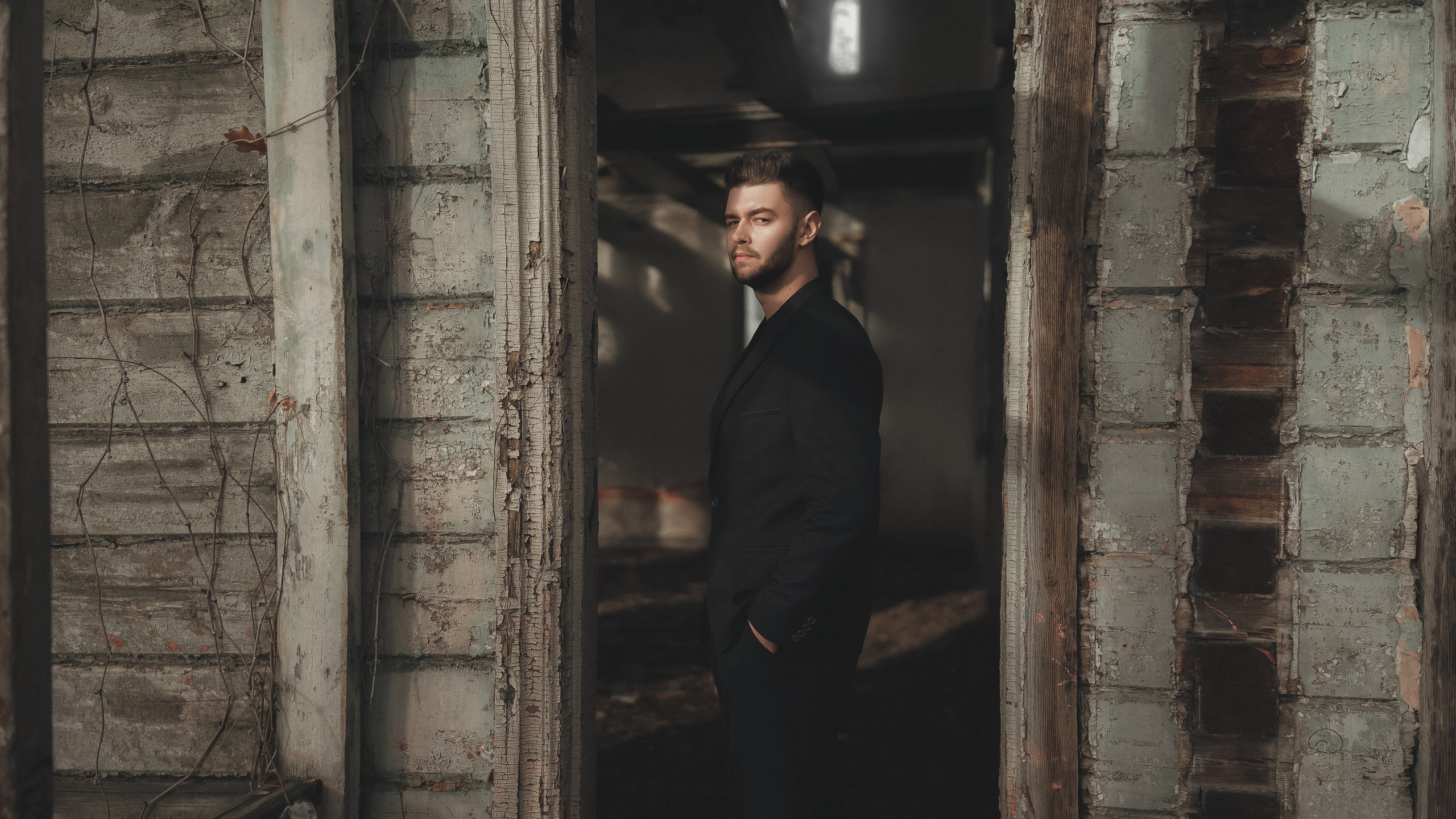 Парень в черном строгом костюме стоит на улице между створок дверей.