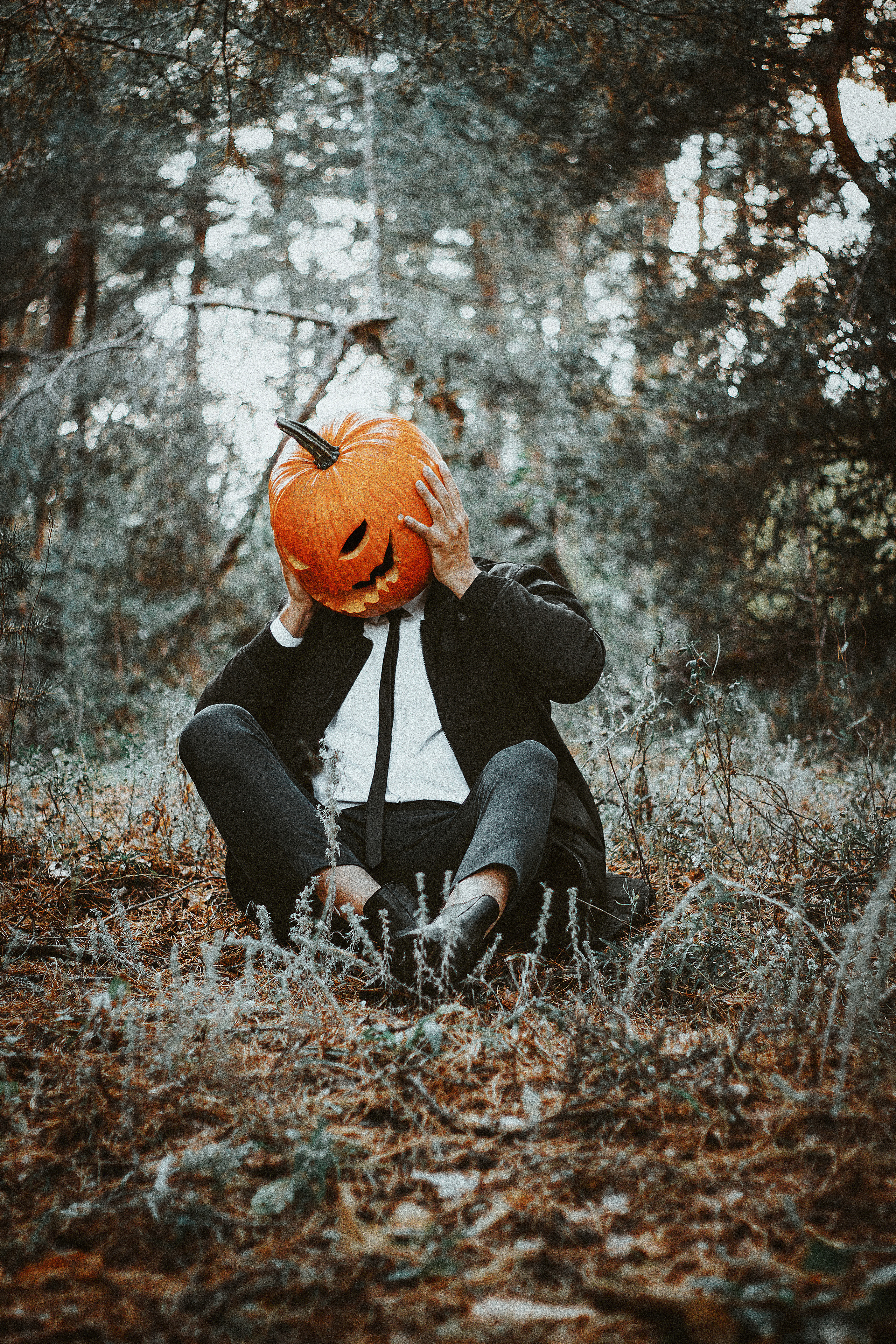 Парень в строгом костюме в маске тыквы сдержится за голову