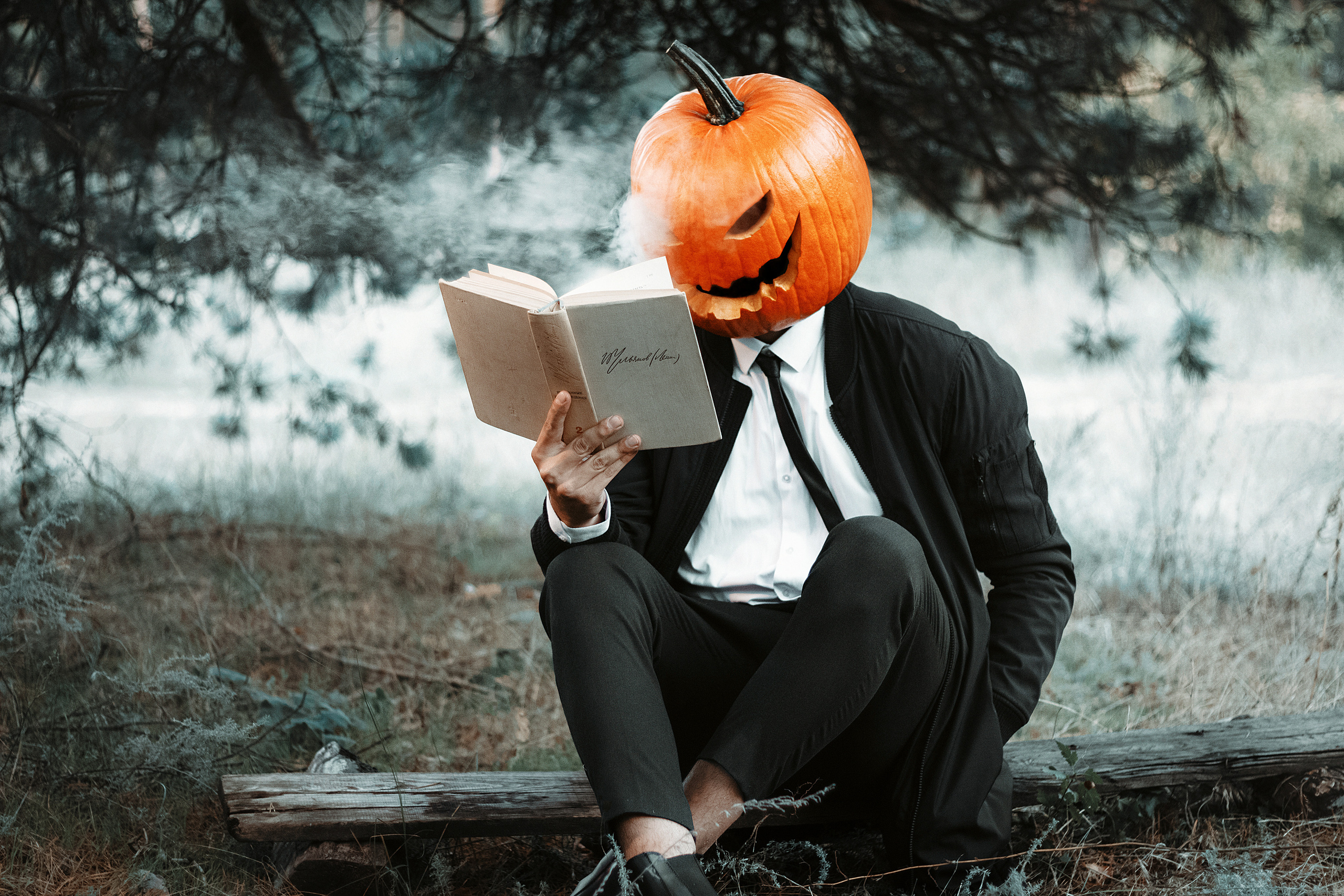 Парень в строгом костюме в маске тыквы читает книгу. Фотограф в городе Воронеже