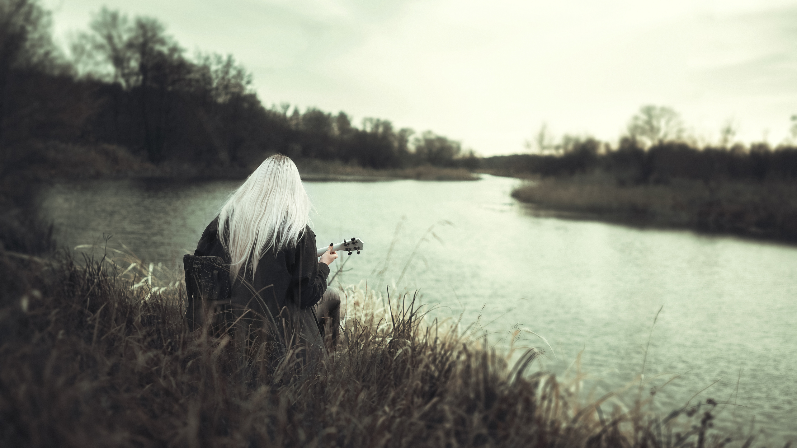 Девочка блондинка с укулеле у берега реки играет красивую музыку 