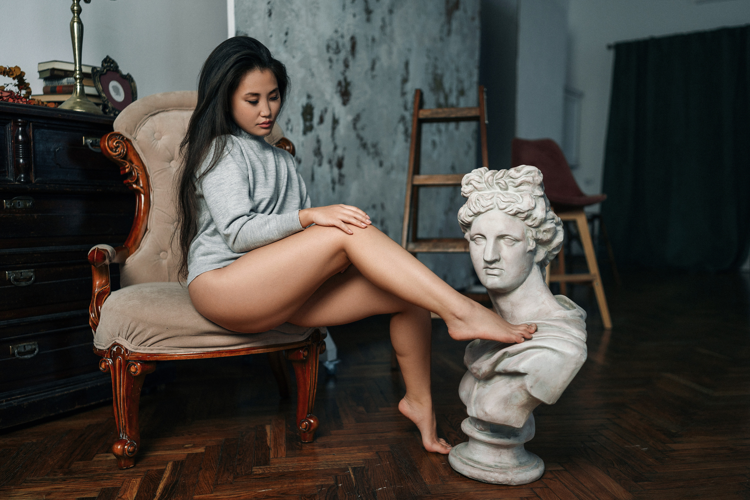 Девушка с азиатской внешностью в серой кофте и черных трусиках положила ногу на бюст римляна
