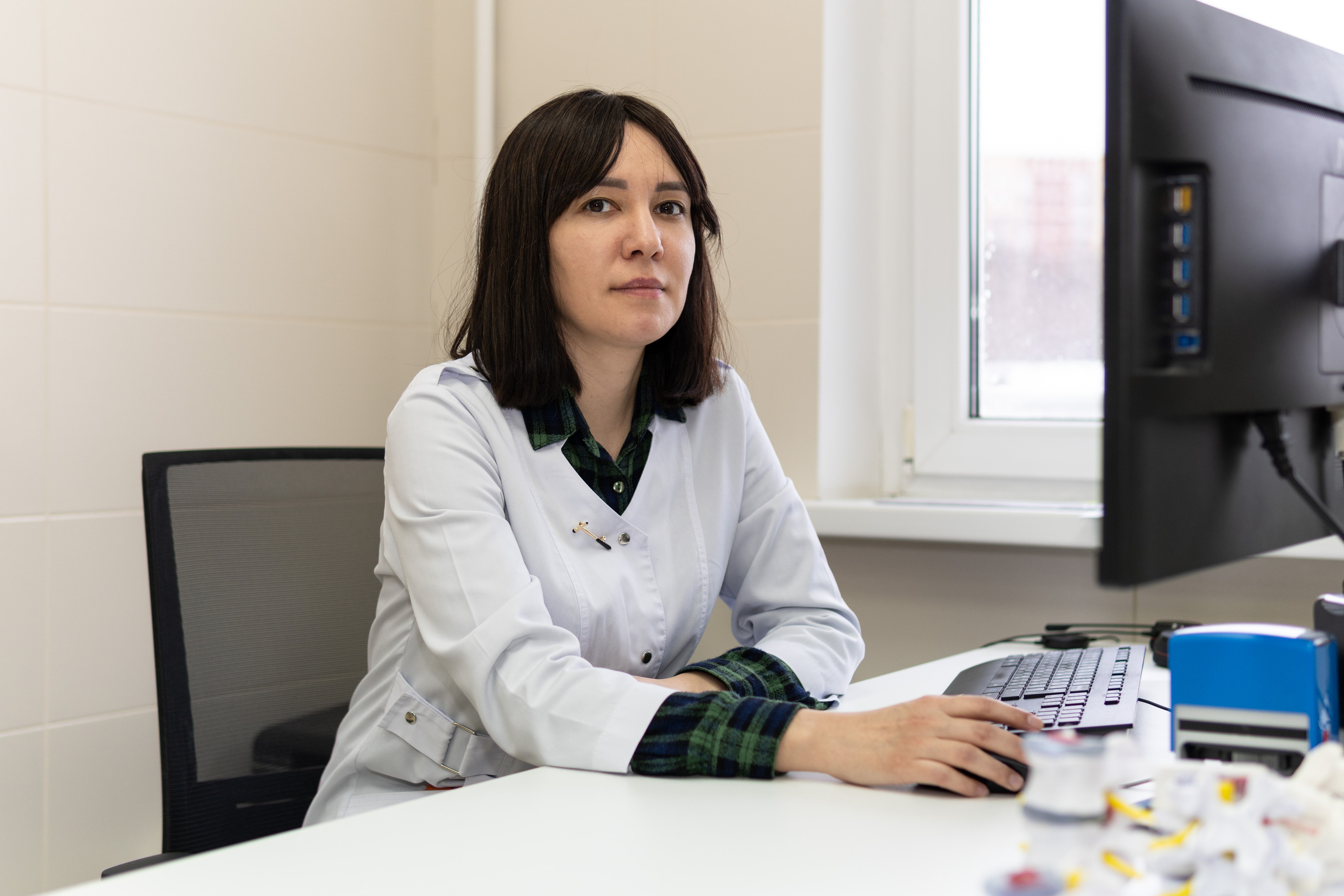 Женщина врач сидит за столом перед монитором