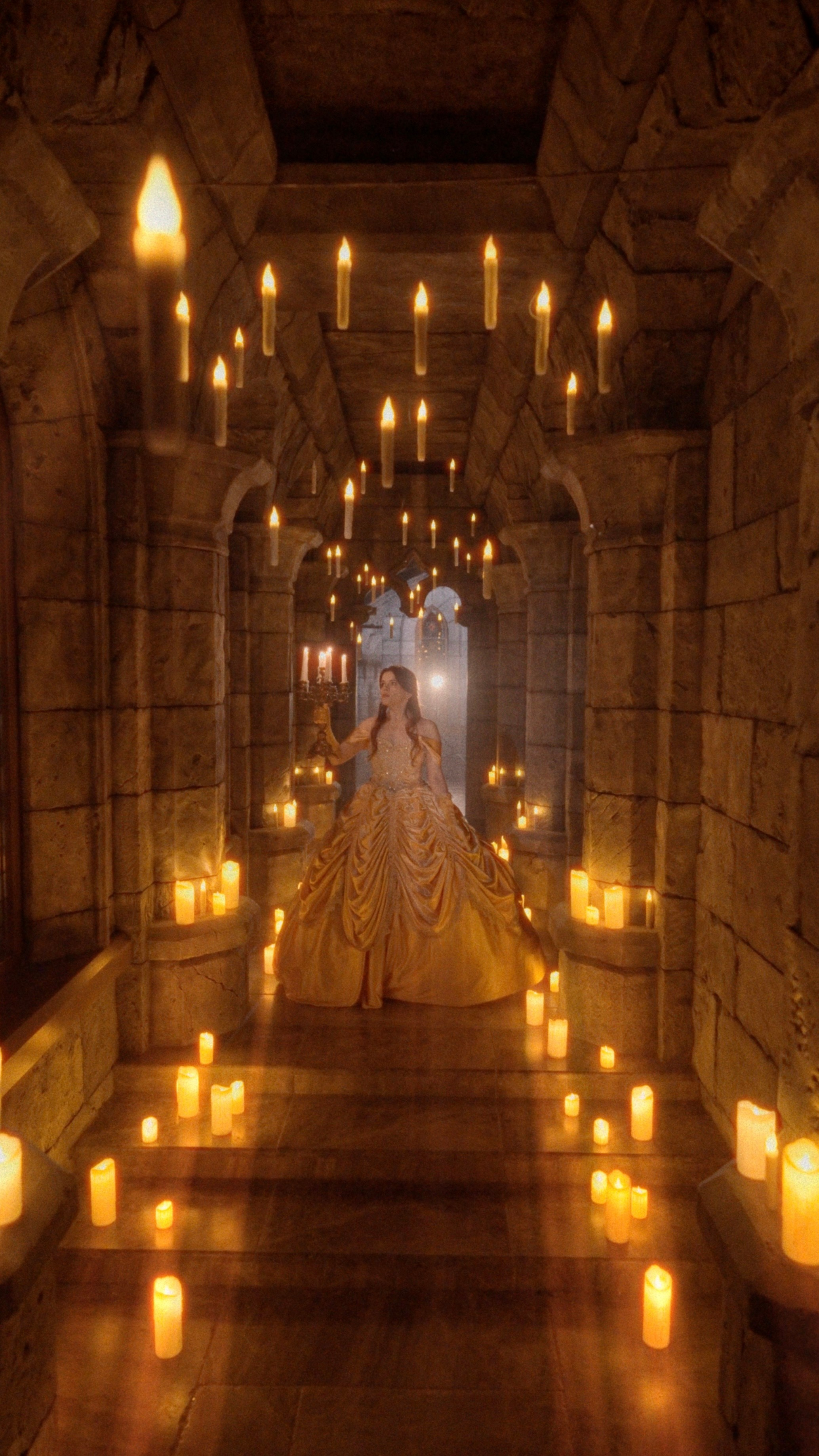 Девушка в золотом бальном платье идёт по коридору, освещённому множеством свечей, создавая волшебную атмосферу замка Гарибальди.