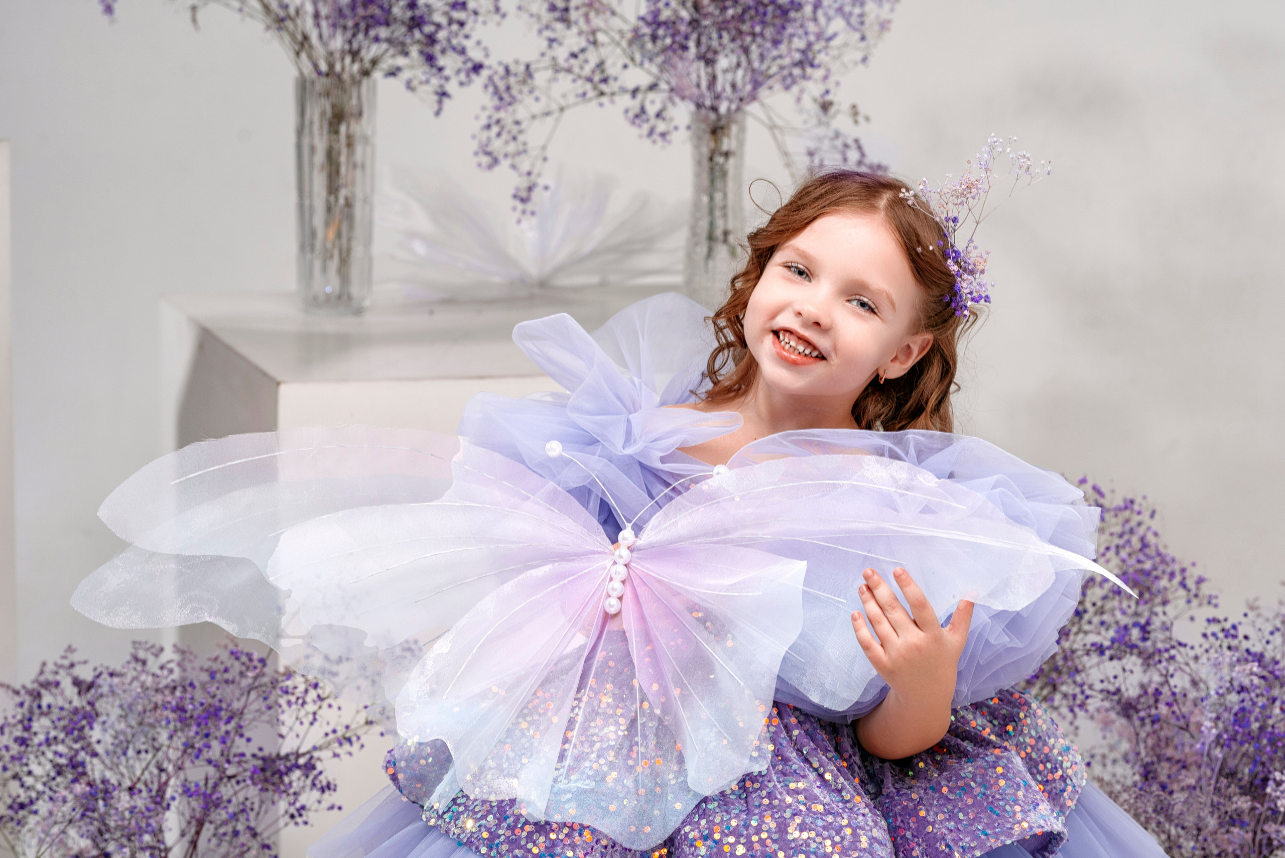 девочка в фиолетовом платье в фотостудии с гипсофилой и большой бабочкой