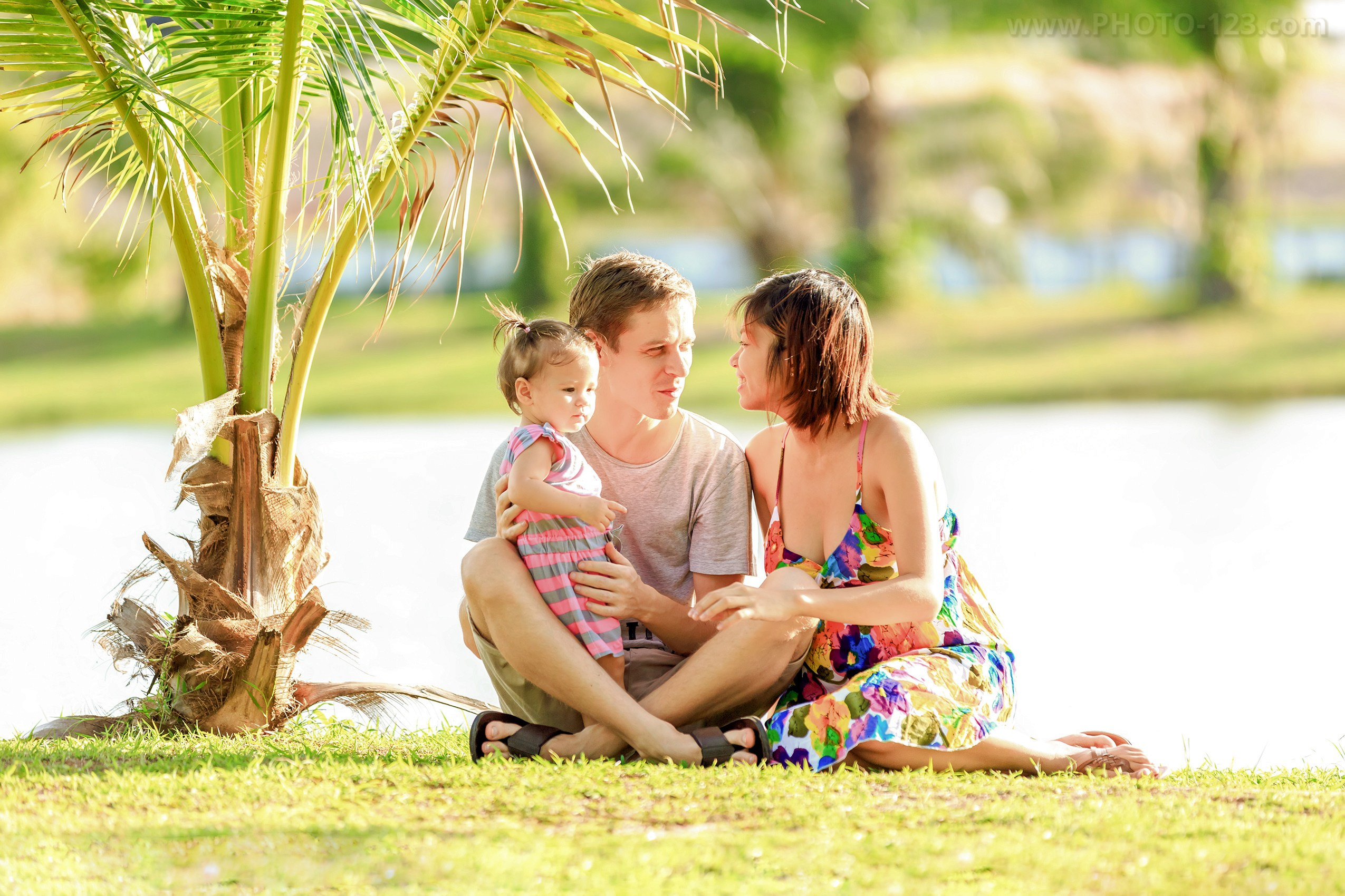 Young family with child sitting under palm tree, lifestyle family photoshoot in Phu Quoc, Vietnam