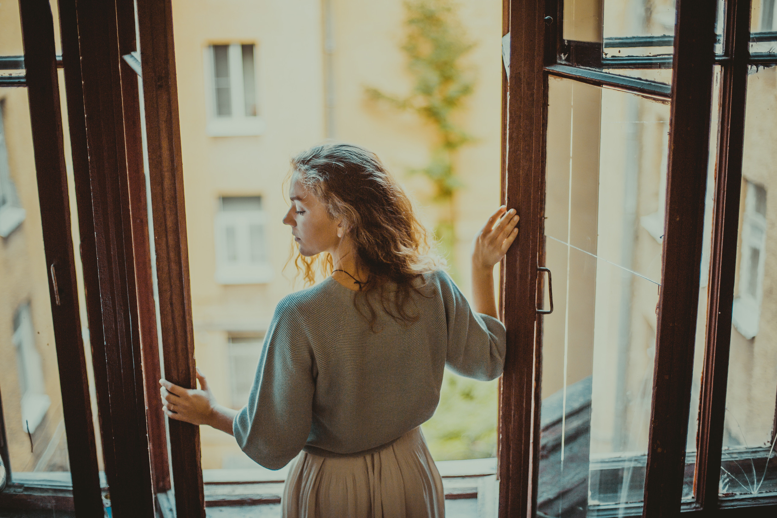 девушка стоит спиной у открытого окна закрыв глаза