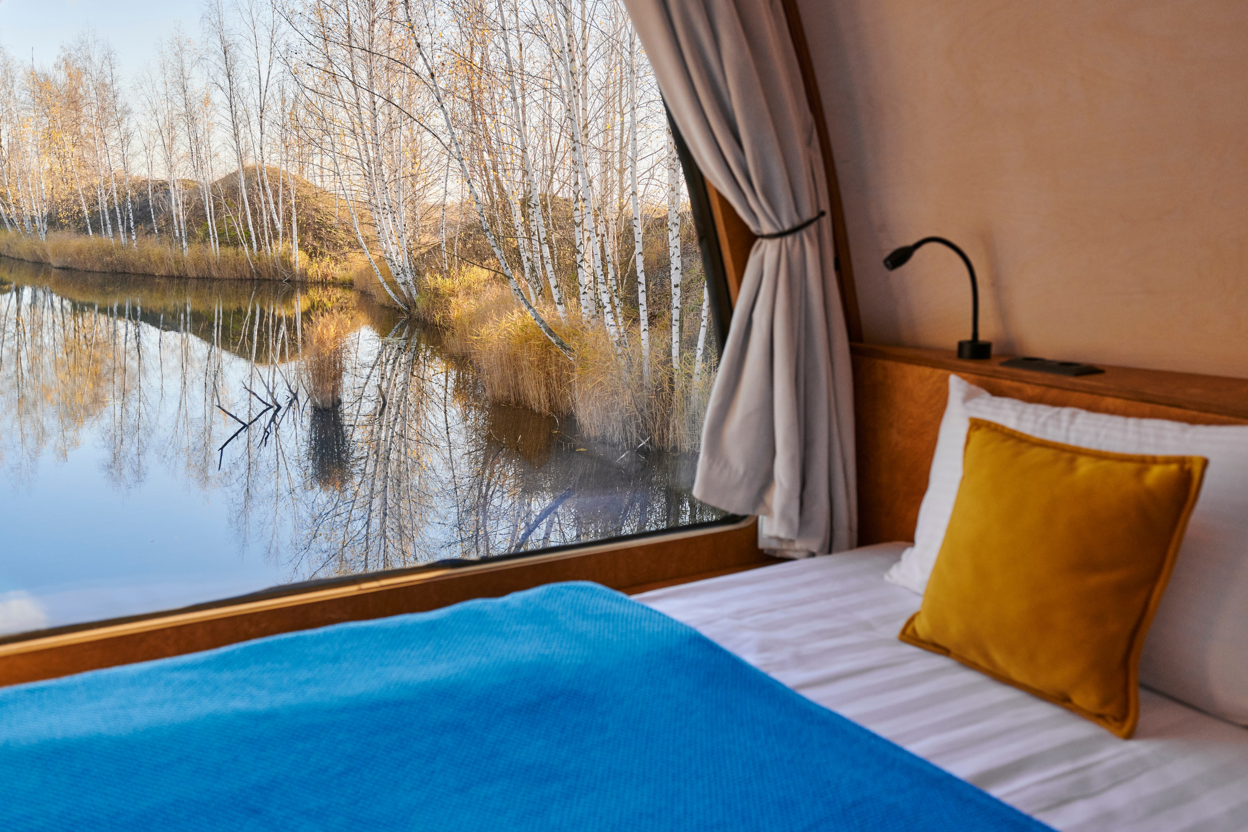 Синий текстиль на кровати, панорама водоёма в окне.