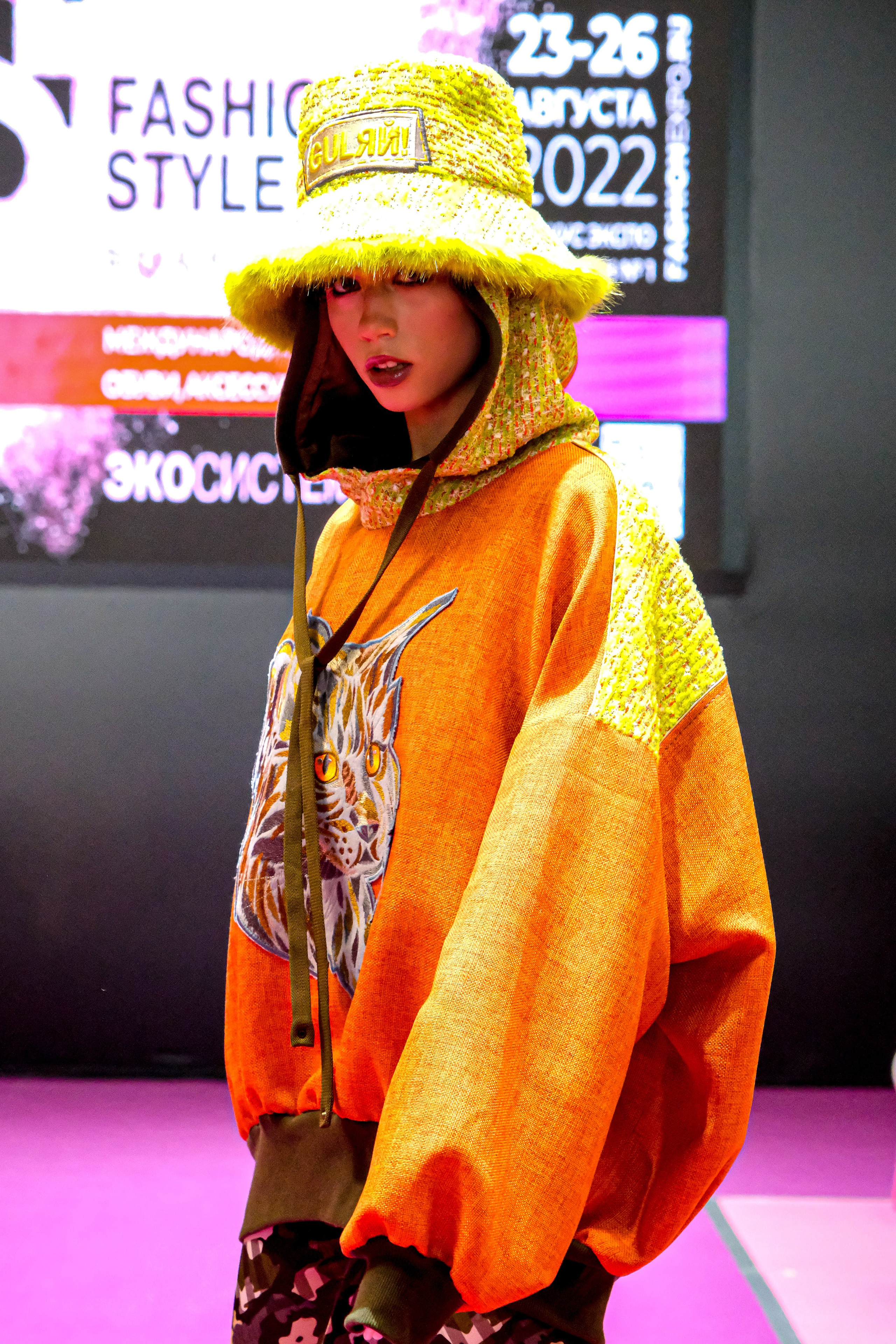  "Модели в ярких нарядах проходят по подиуму во время показа мод, освещенные яркими софитами и окруженные восторженными зрителями."