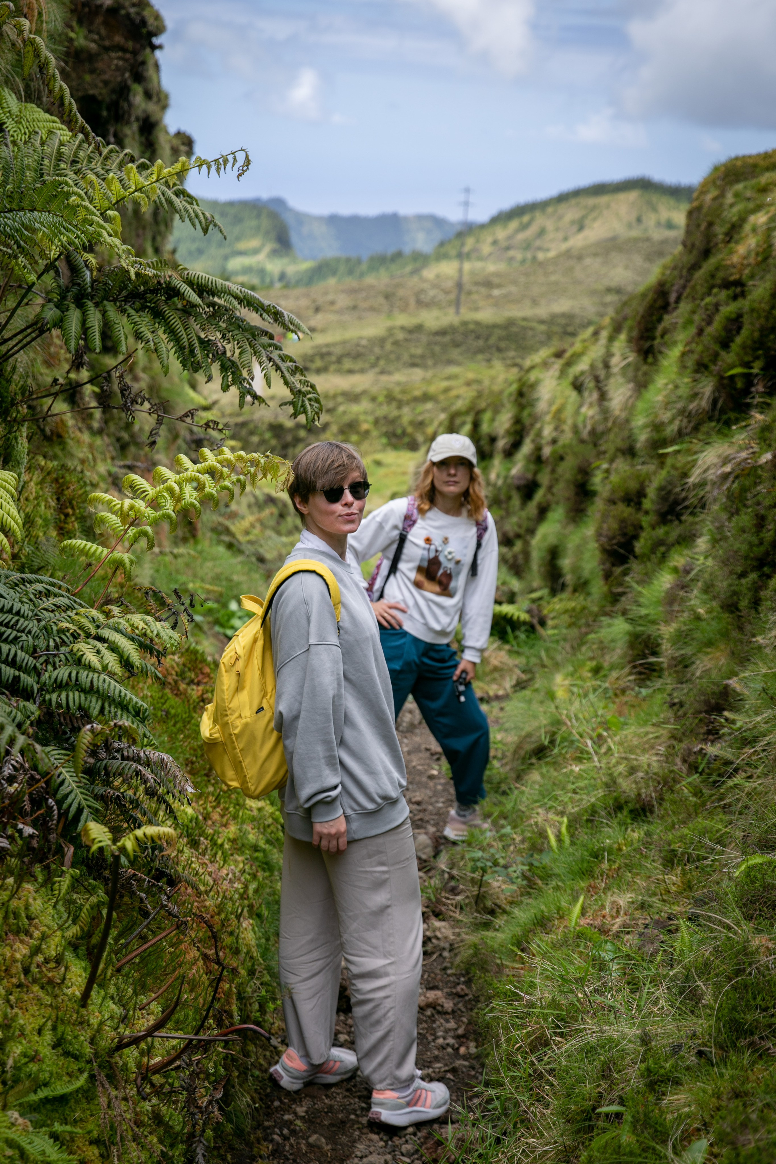 A group of young women walking through lush green landscapes, with the vast ocean and clear blue sky surrounding them on the Azores