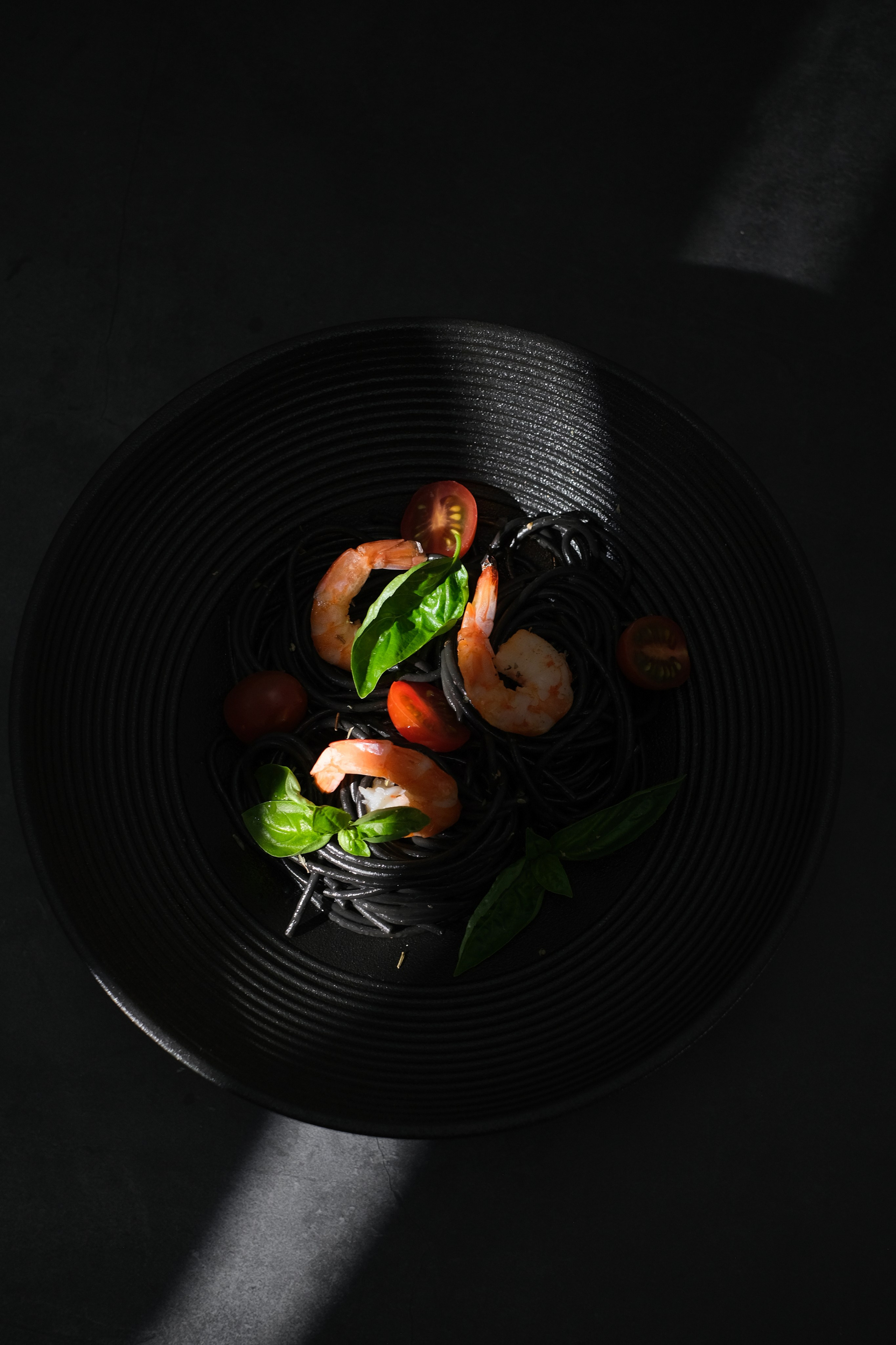 Фотография тарелки с черным спагетти и креветками 