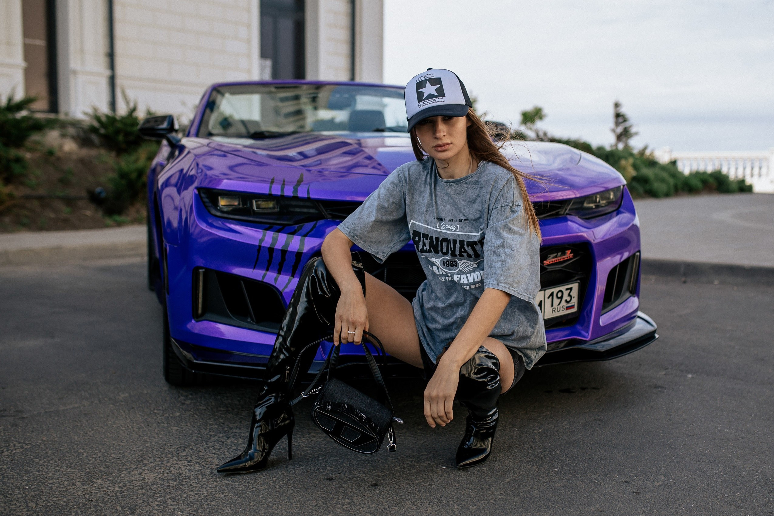 Стильная девушка в сапогах у роскошного автомобиля на фоне моря Анапы.