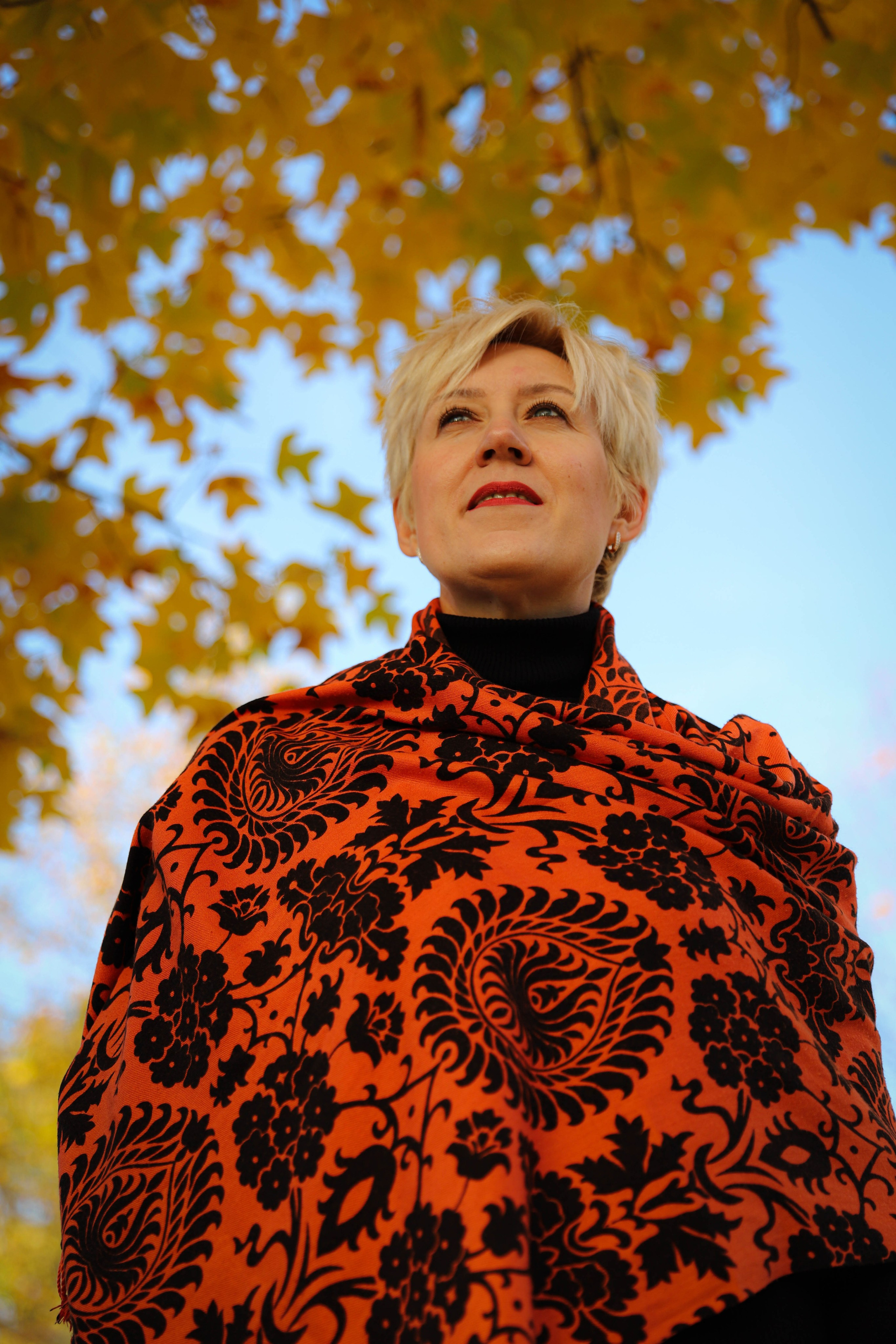 Красивая девушка в оранжевом платке стоит под деревом с падающими листьями в парке Краснодар