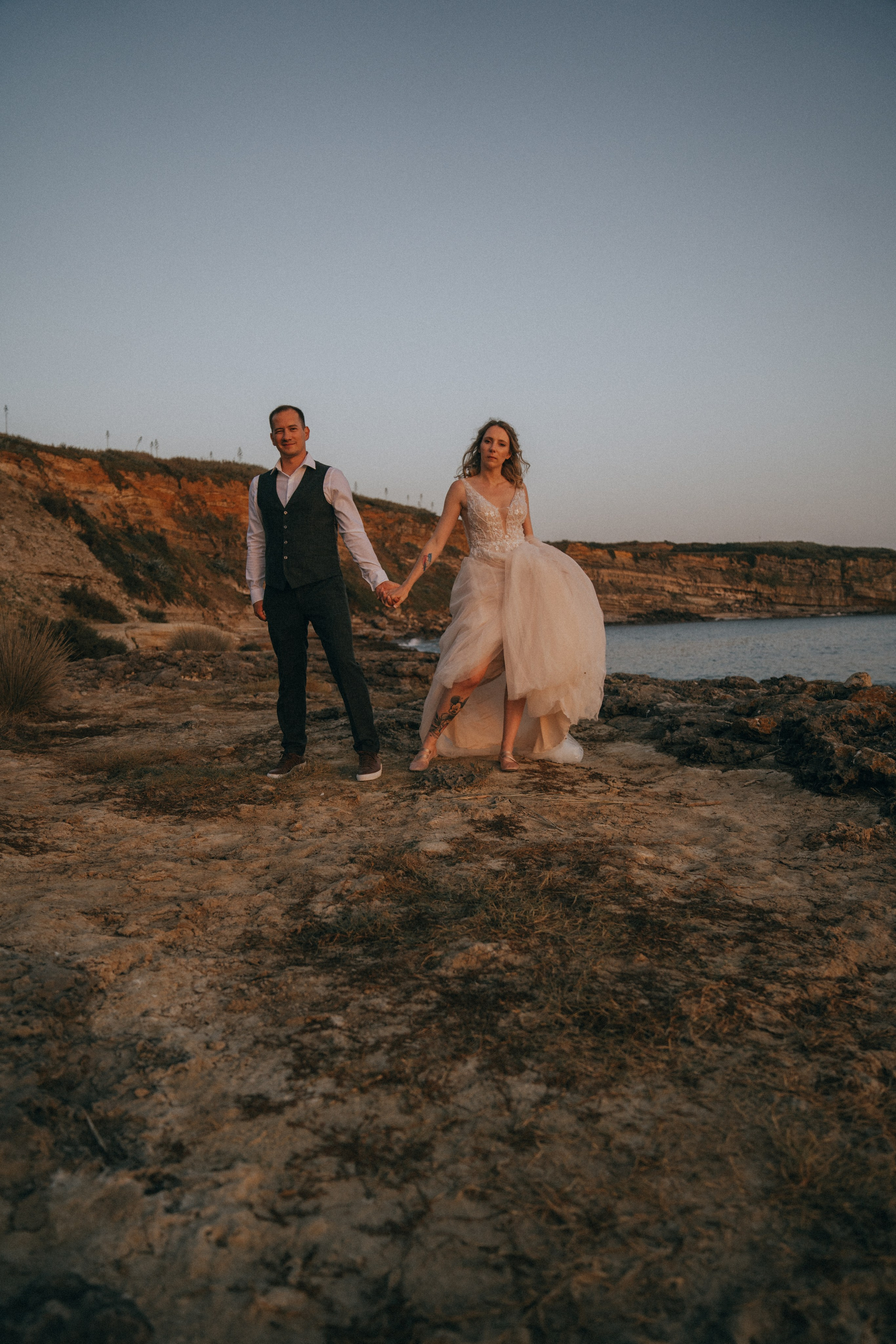 Счастливая пара жених и невеста целуется на фоне волн  скал и заката у моря океана.