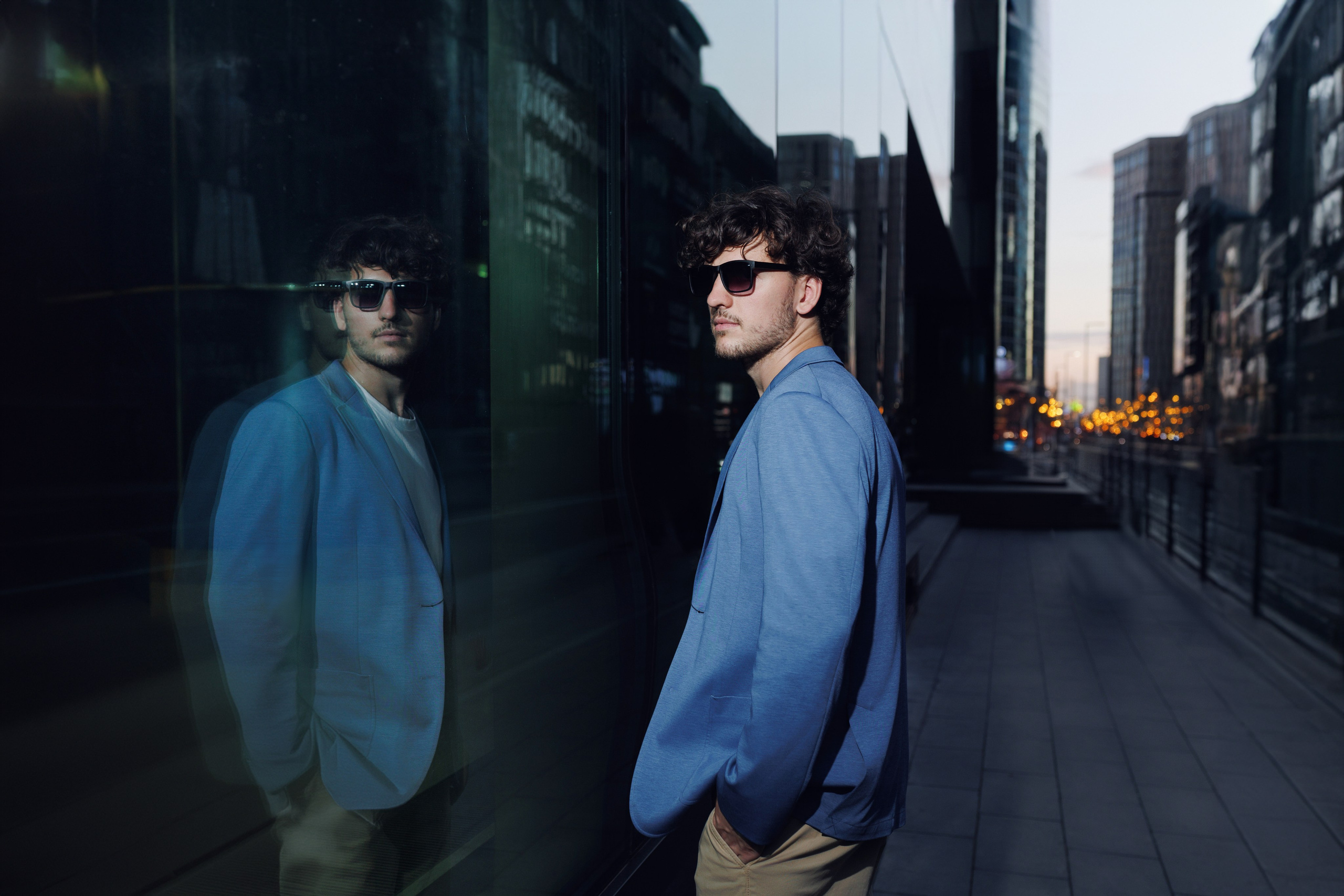 Архитектурный портрет: отражение бизнесмена в стекле фасада на фоне силуэтов небоскрёбов Москва-Сити и закатного неба. Креативная композиция.