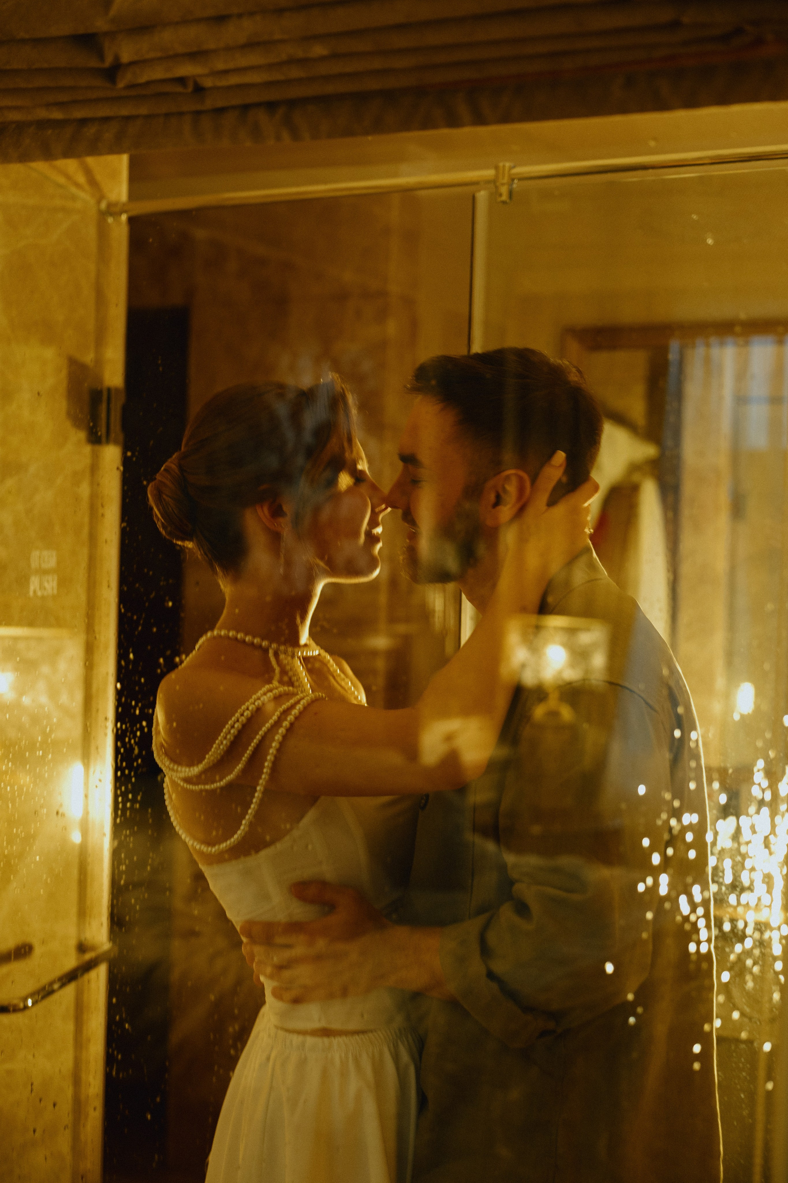 Жених и невеста целуются, их отражение видно в зеркале, освещенное золотистым светом.