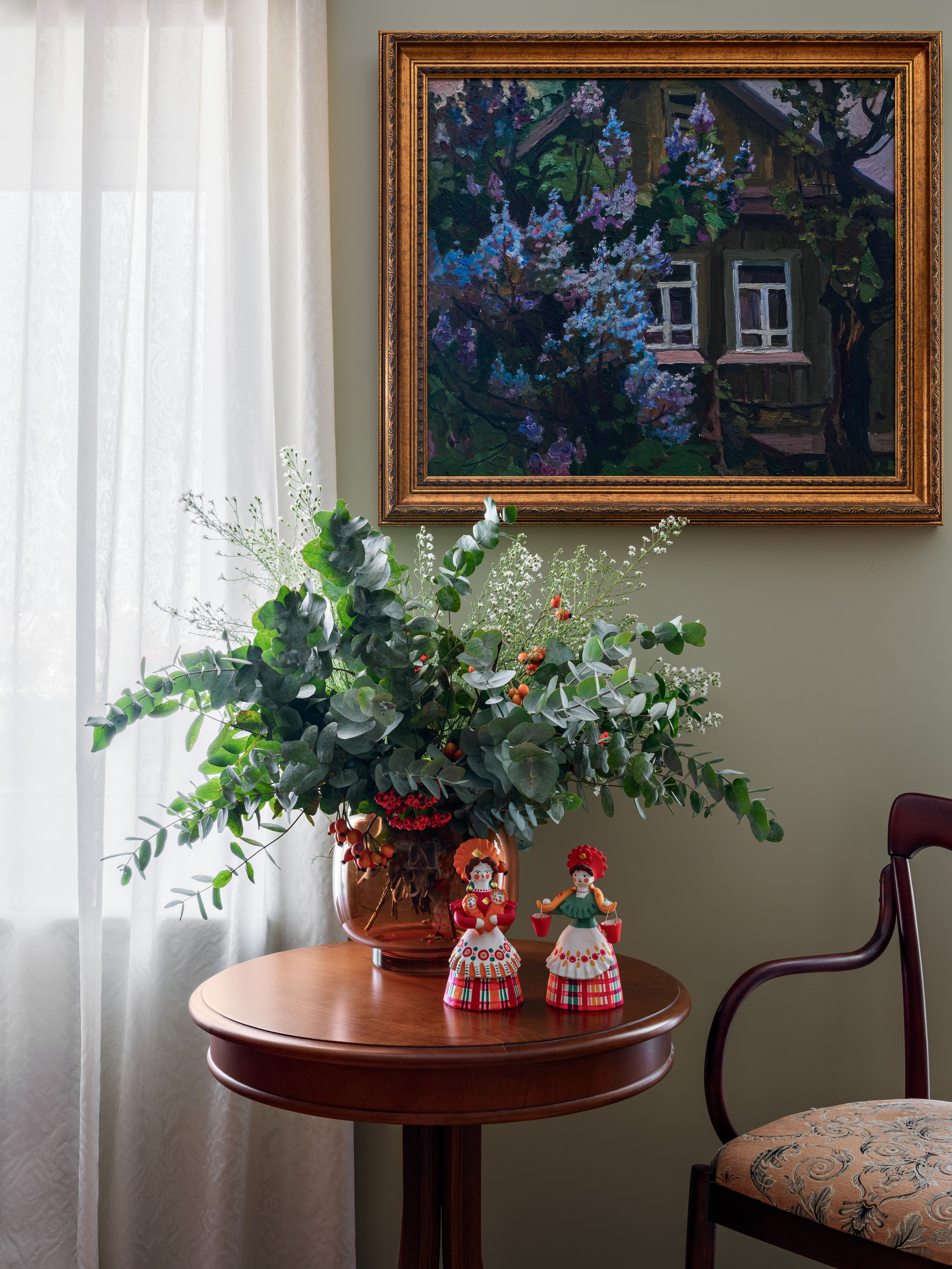Элегантный интерьер с круглым столиком из массива дерева, вазой с цветами и декоративными фигурками, на фоне зелёной стены и картины в раме; сочетание традиций и уюта. Проект Юлии Капункиной и Альбины Терещенко, стилист Алина Нелень, фотограф Сергей Денисенко.