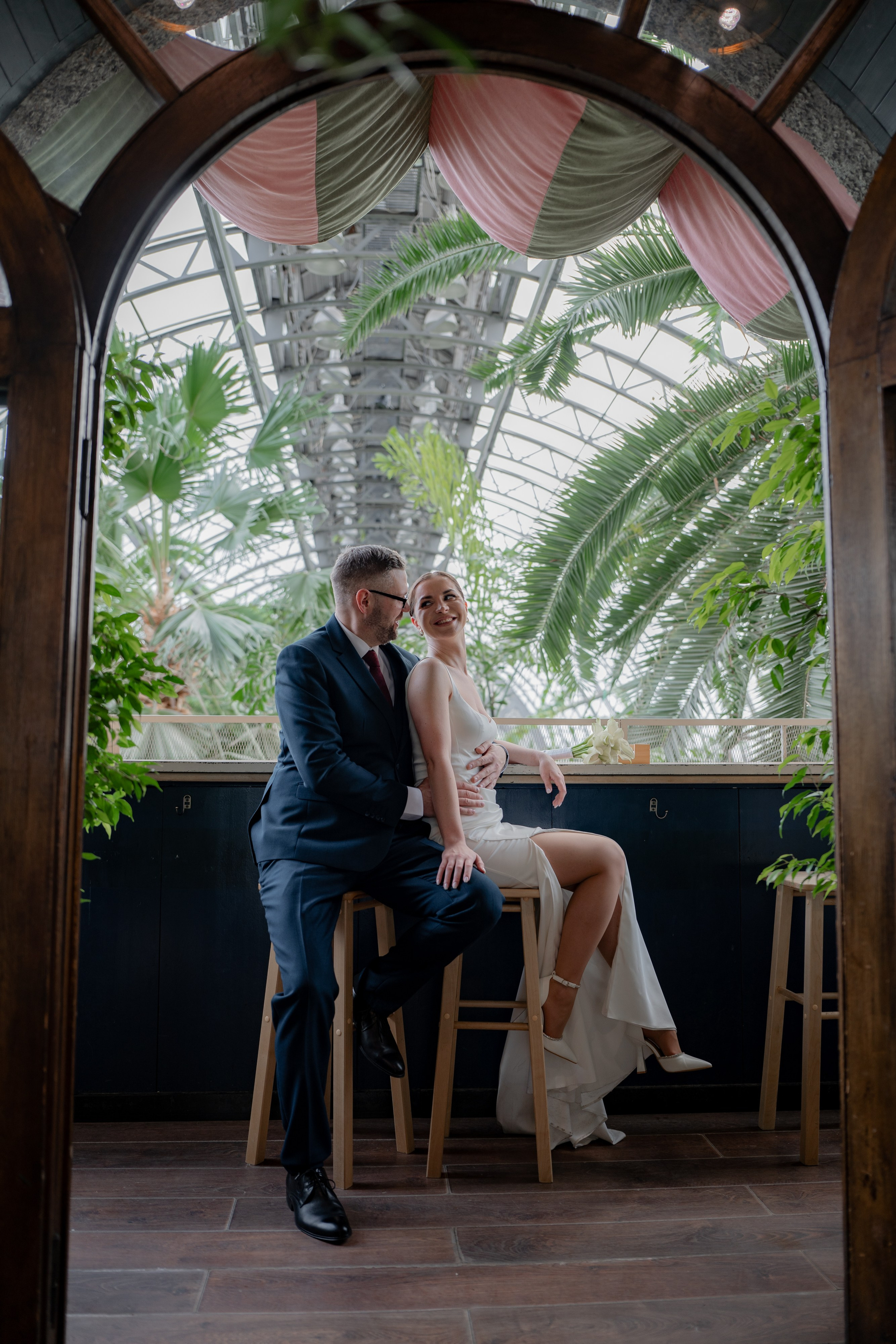Свадебная фотосессия в оранжерее Таврического сада. Жених и невеста сидят в кафе на втором этаже на стульях и обнимаются