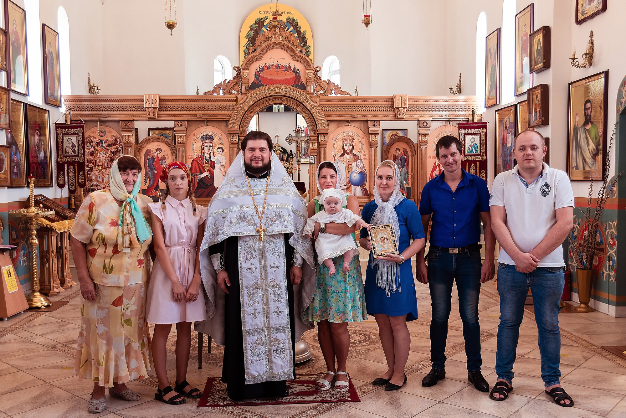 Общий фотоснимок семьи со священником в храме во время крещения младенца