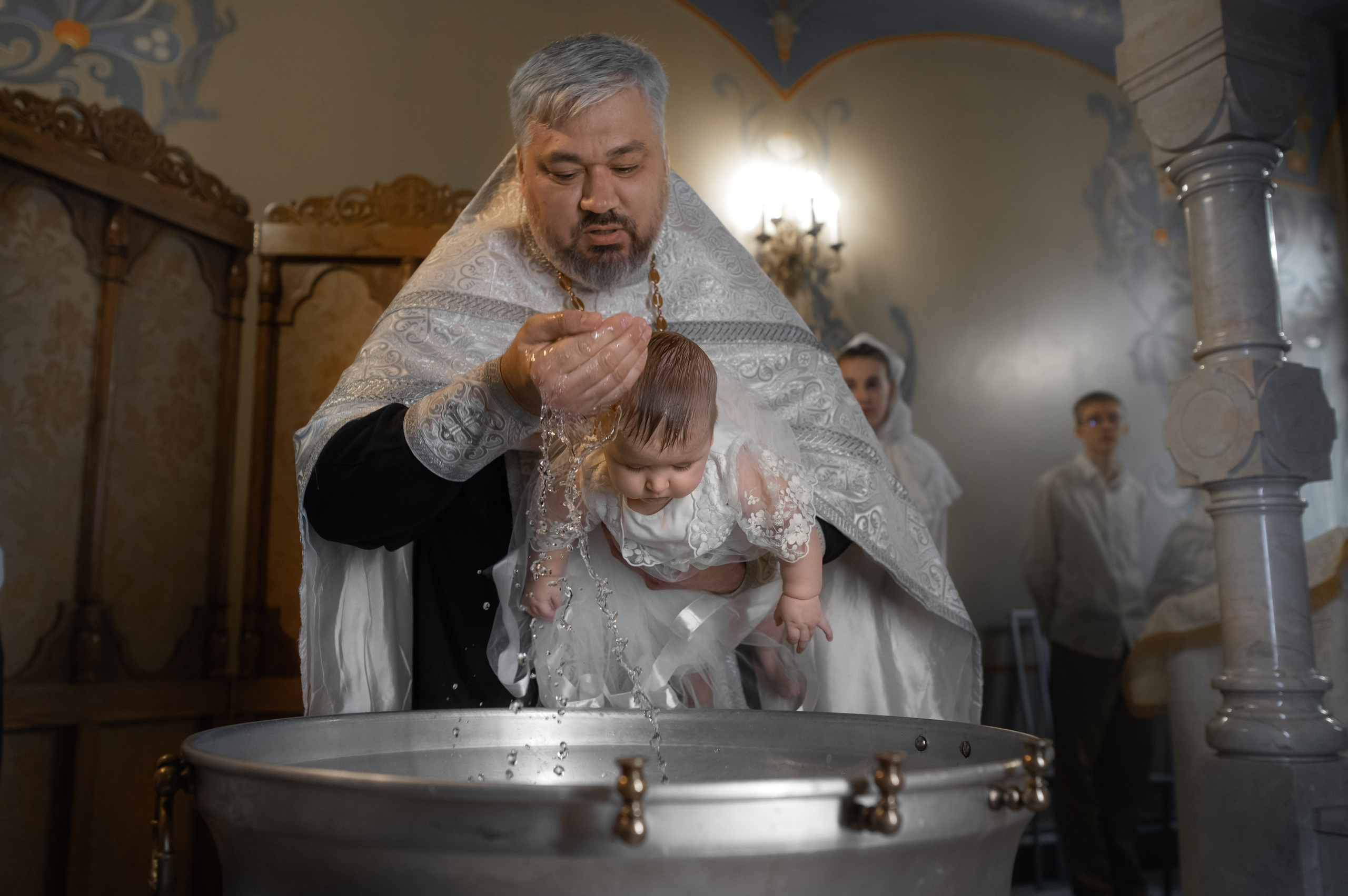 батюшка окунает в купель малышку на крещении в Оптинском подворье Санкт-Петербурга