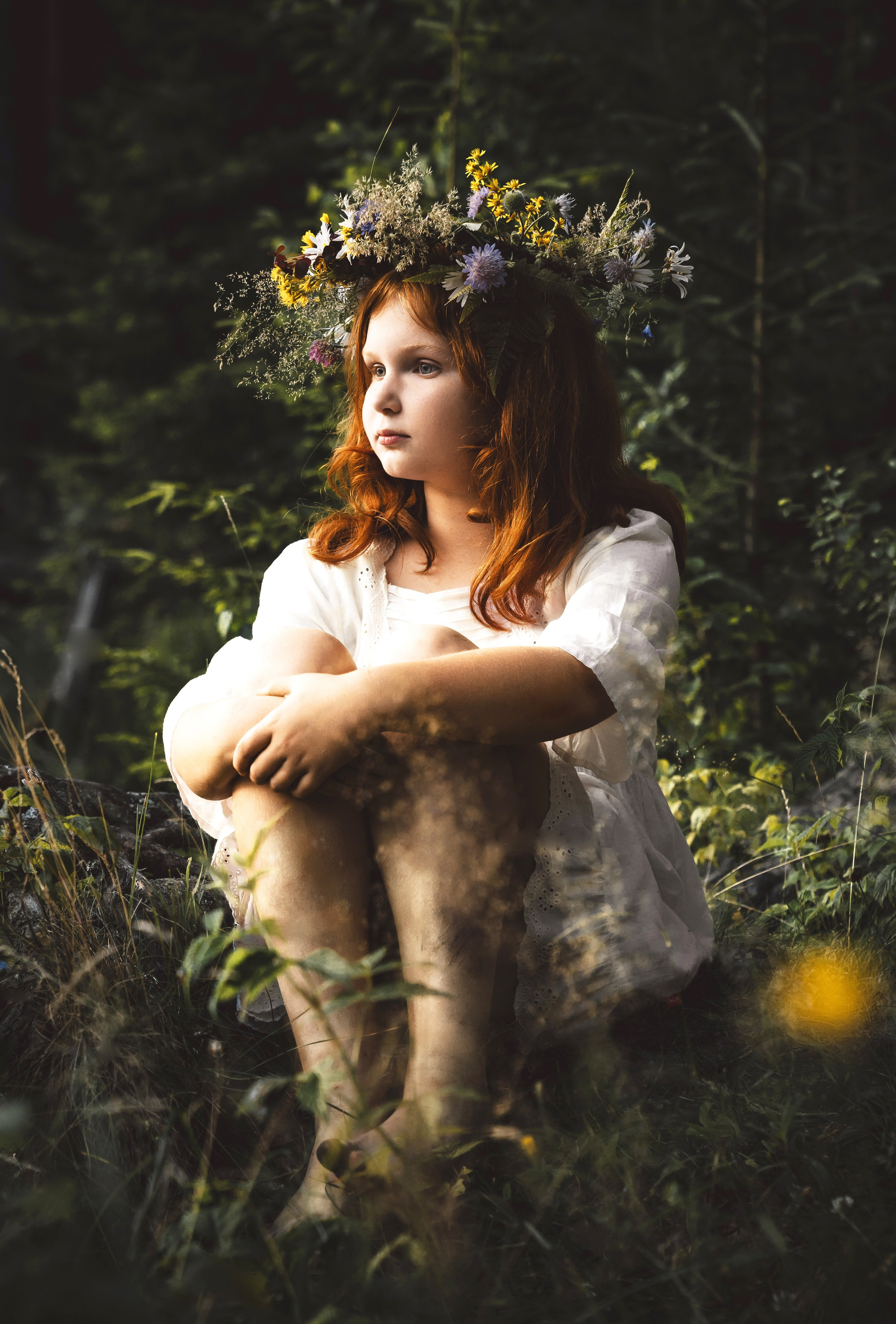 Рыжая девочка с венком из цветов сидит в лесу, задумчивый портрет.