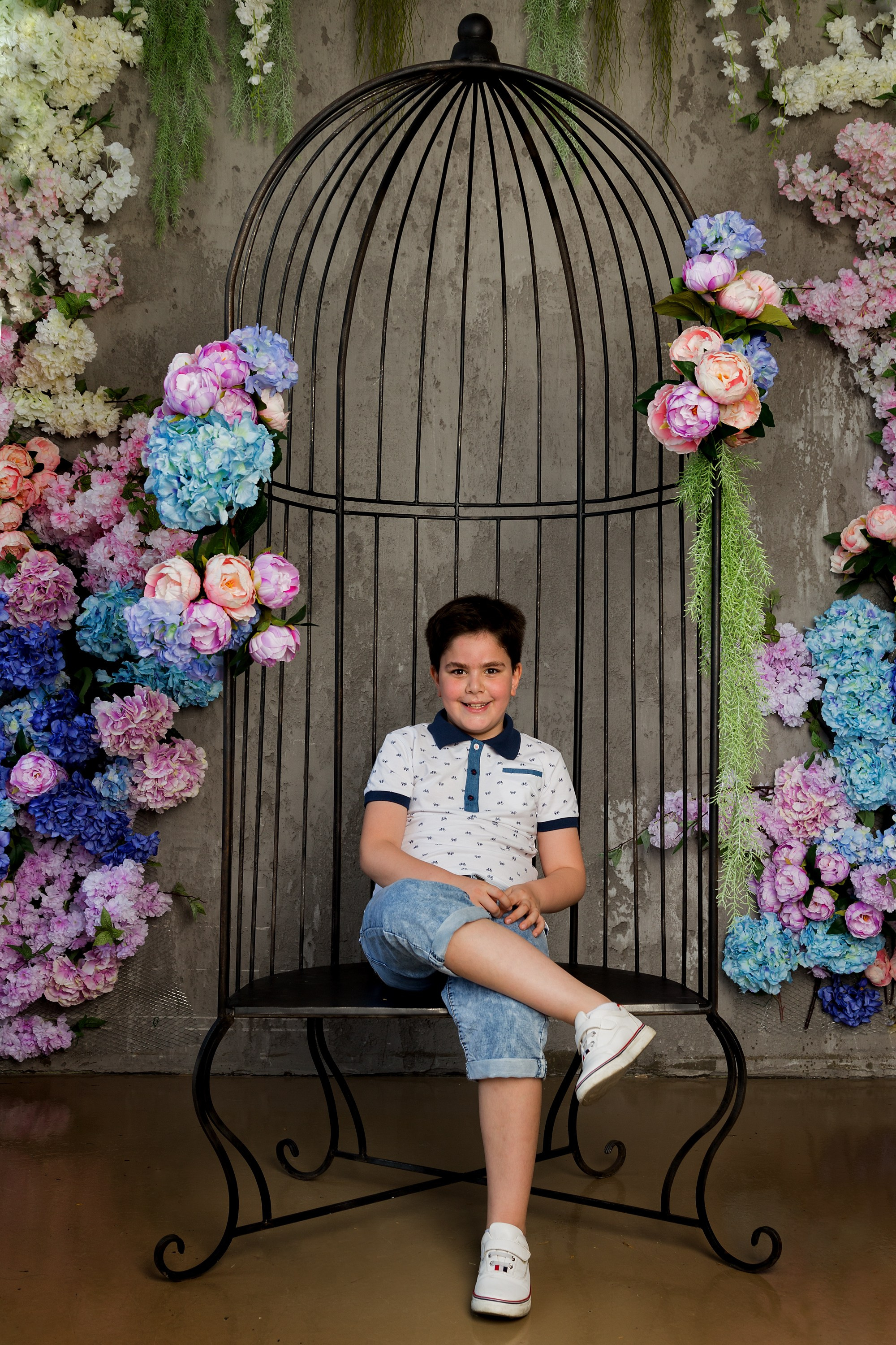 мальчик в цветах на качелях в виде птичий клетки