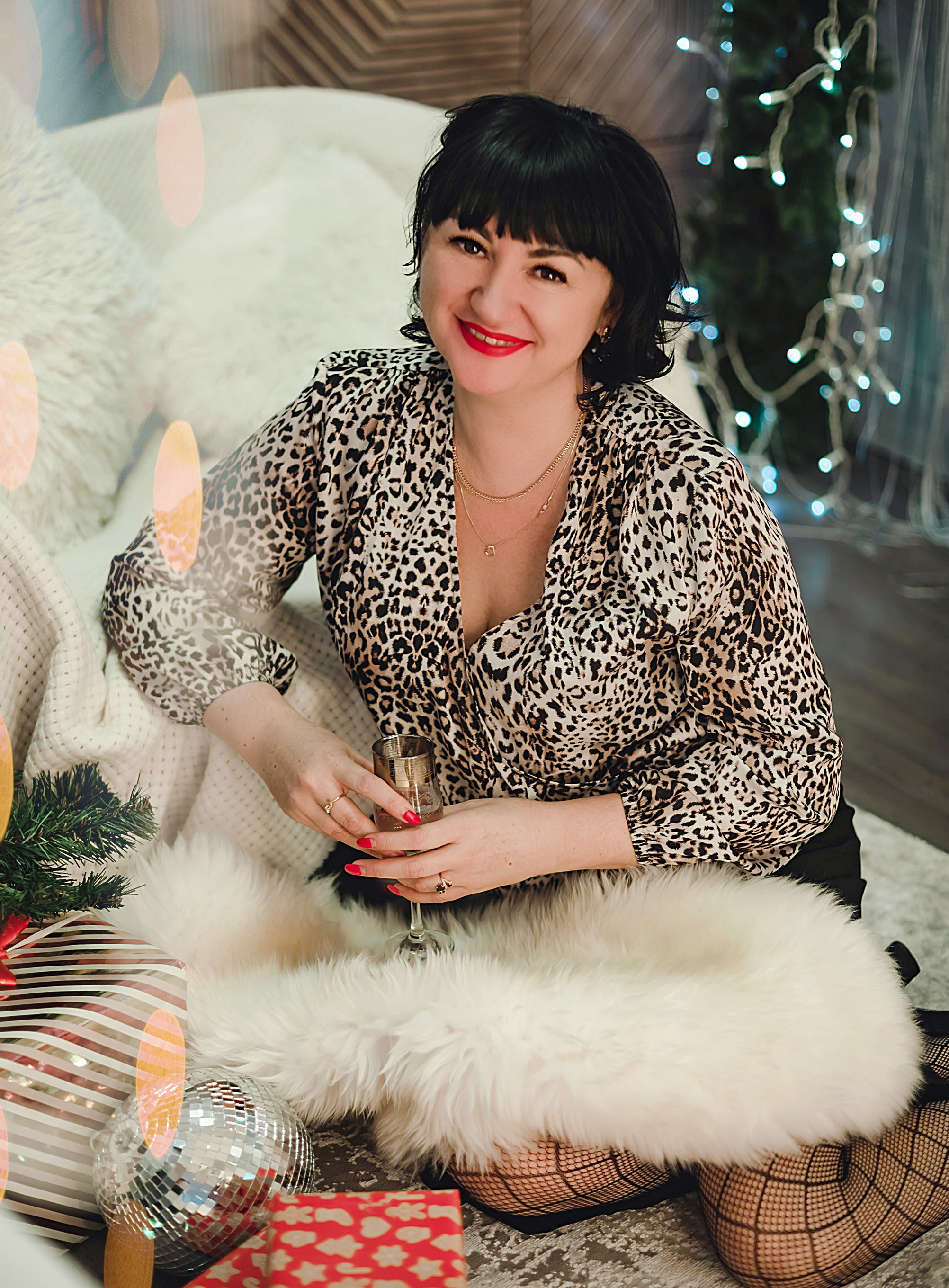 На фото  портрет девушки с подарком сидит около дивана на новый год.