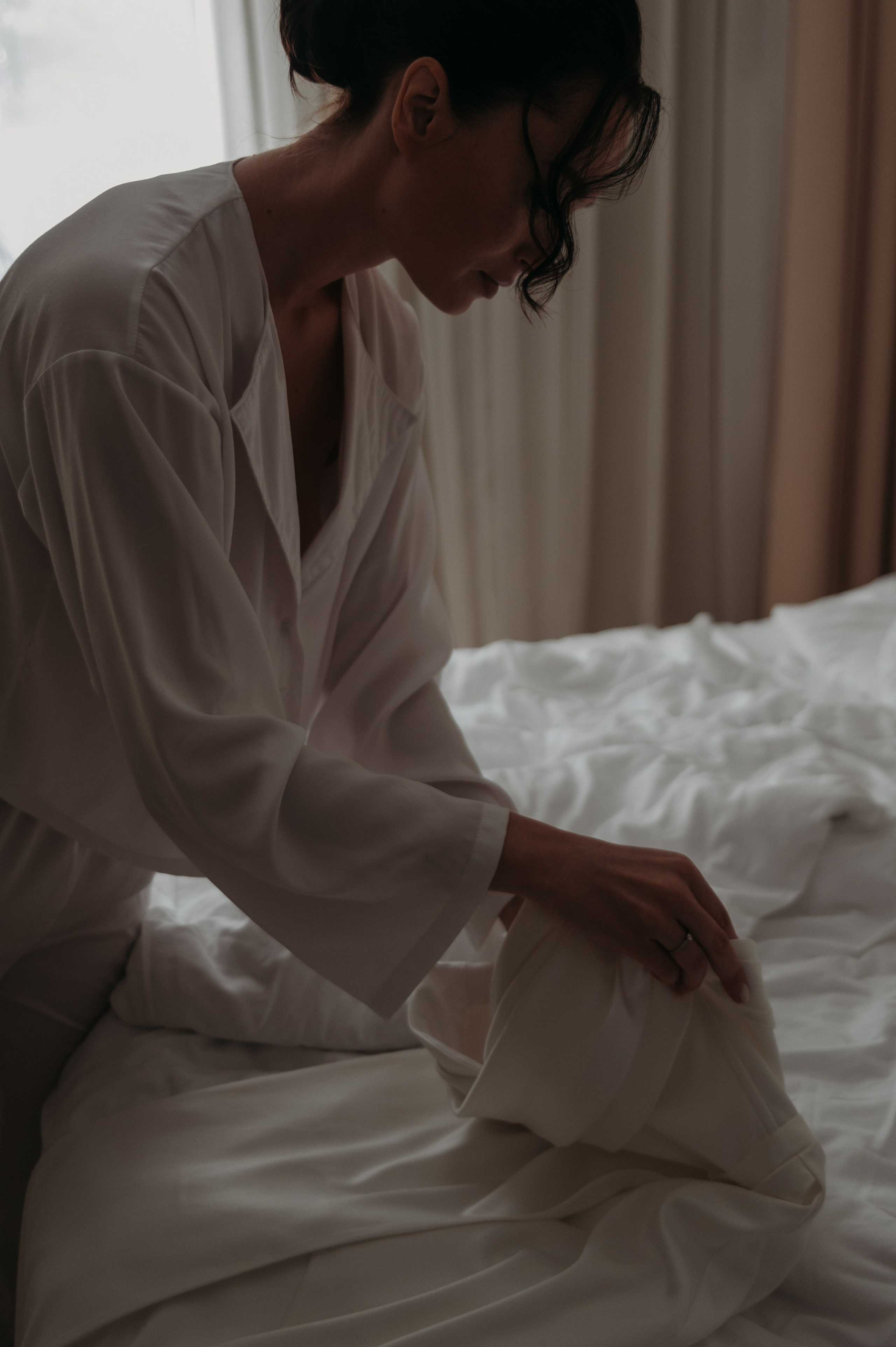 свадебная фотосессия в Твери и Москве: невеста на утро невесты нежно раскладывает белое платье на кровати