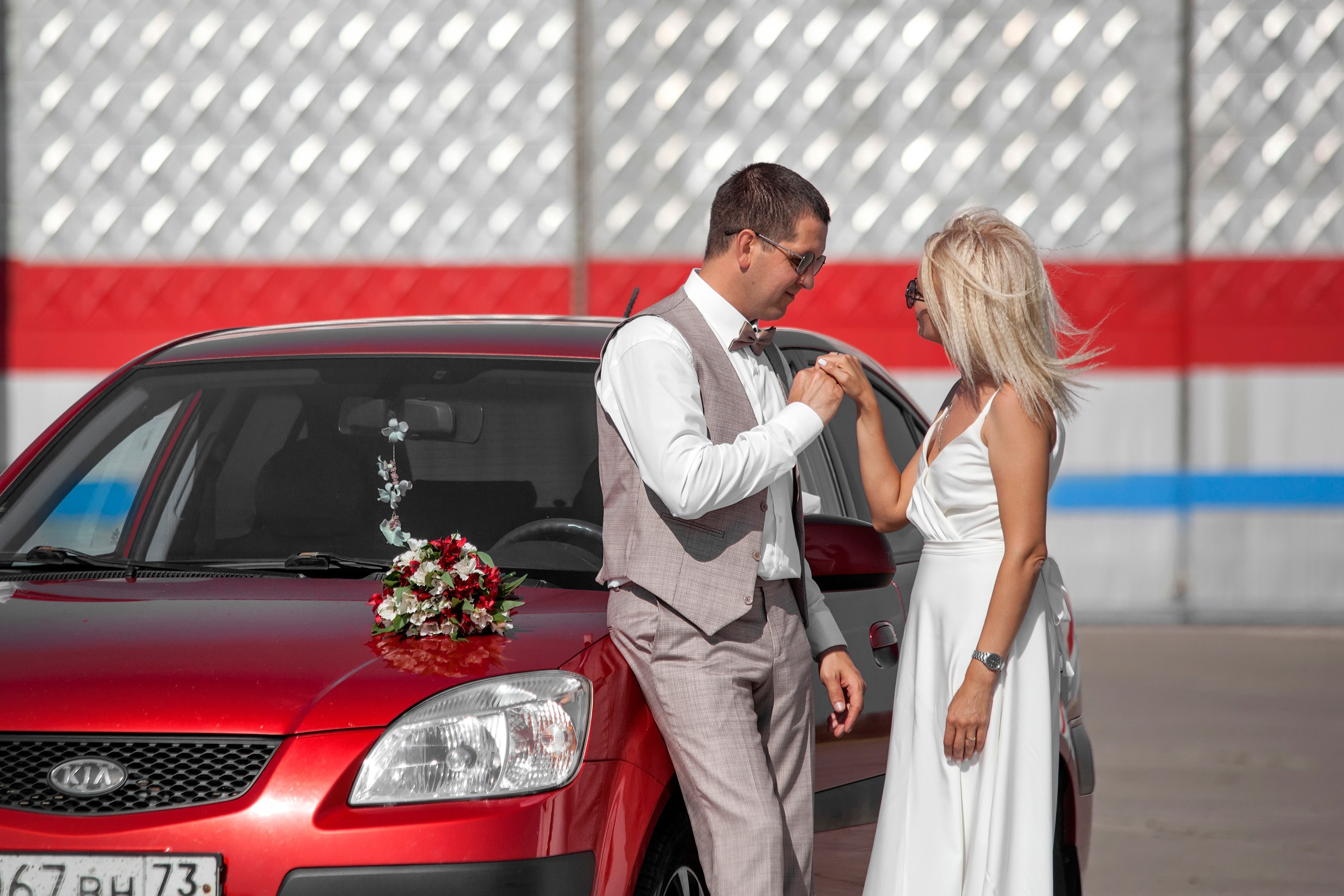 Жених с невестой около красной машины в городе