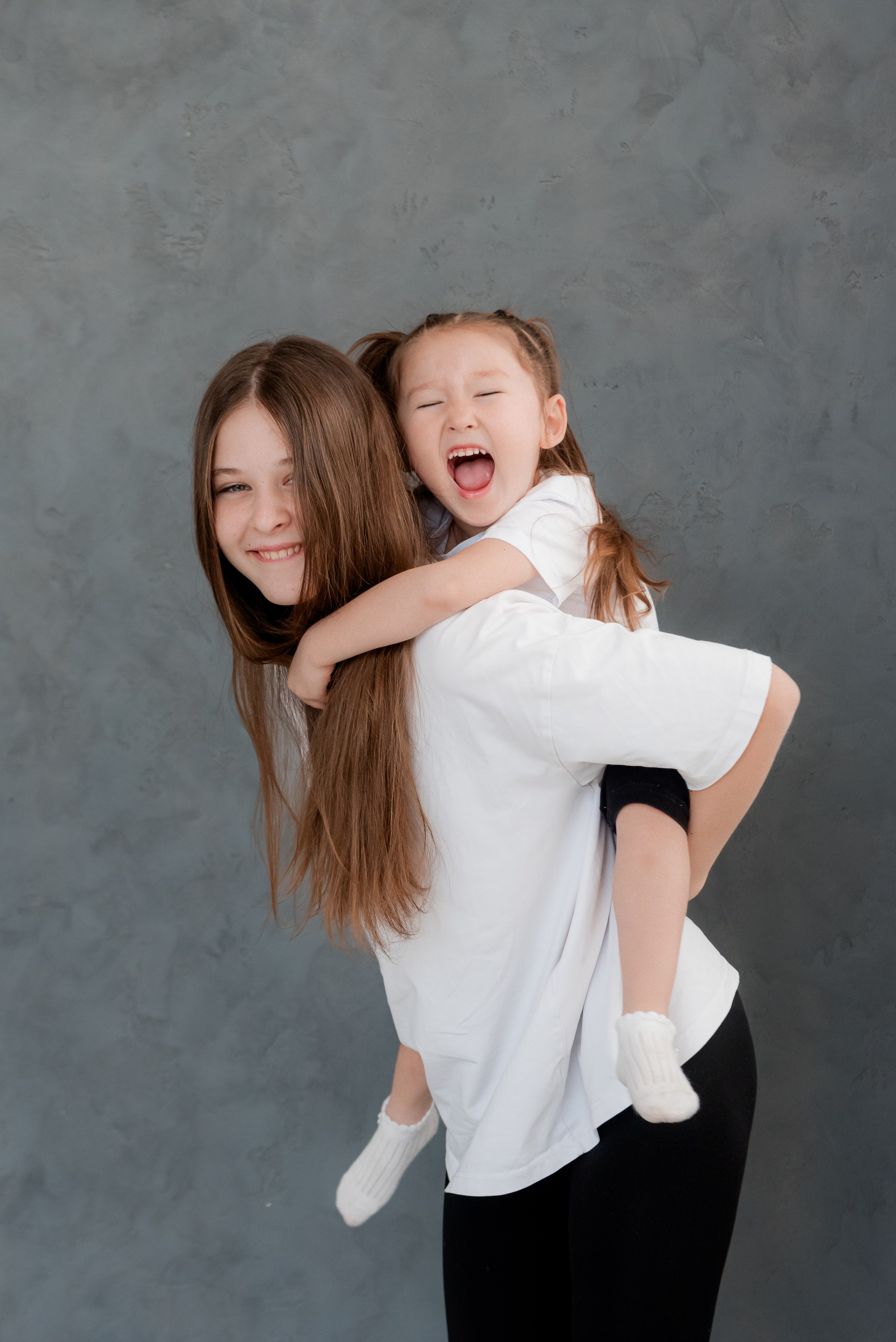 Естественные семейные фото в студии - ребенок заливисто смеется сидя на старшей сестре.