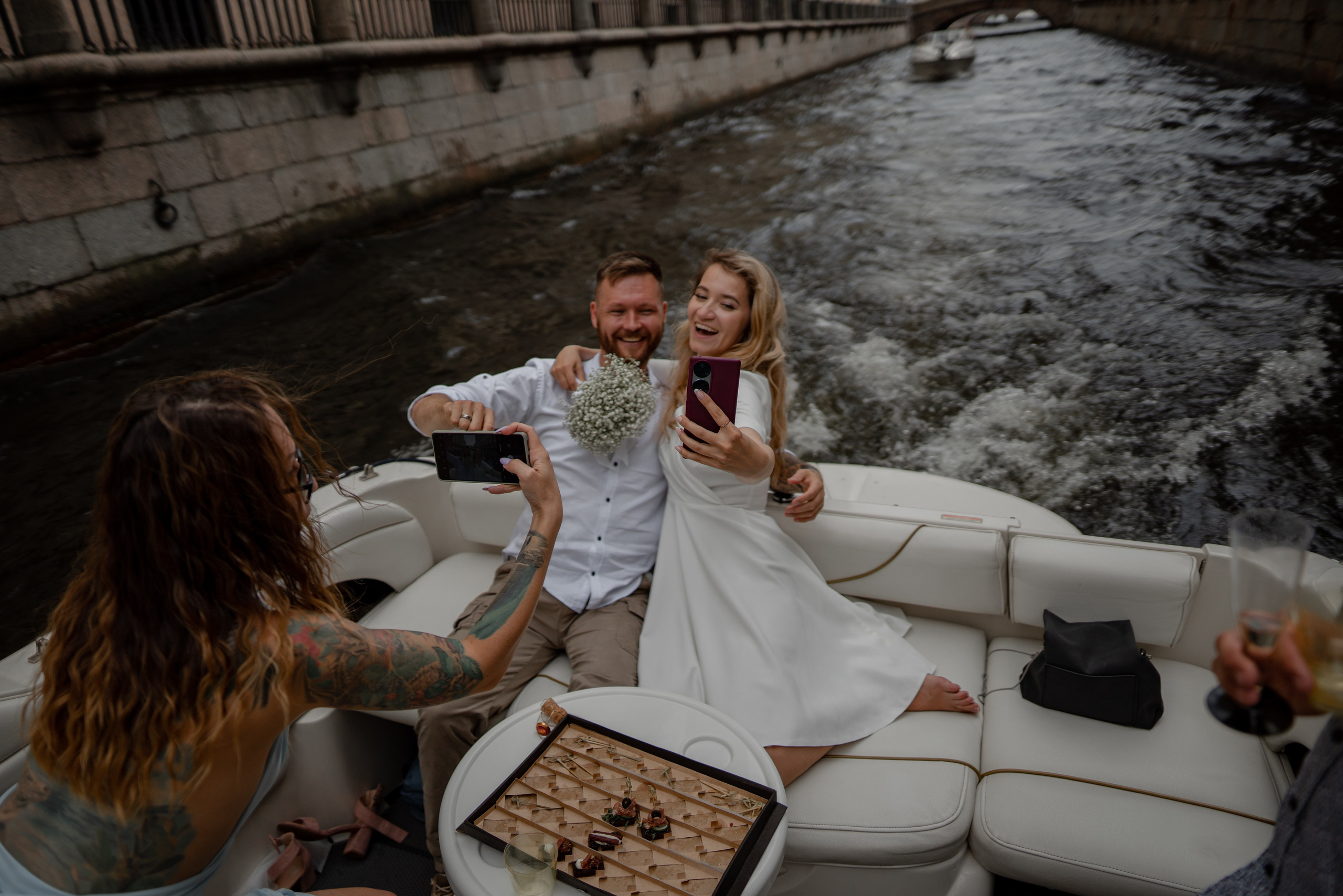 подруга невесты фотографирует жениха и невесту на яхте в каналах Санкт-Петербурга