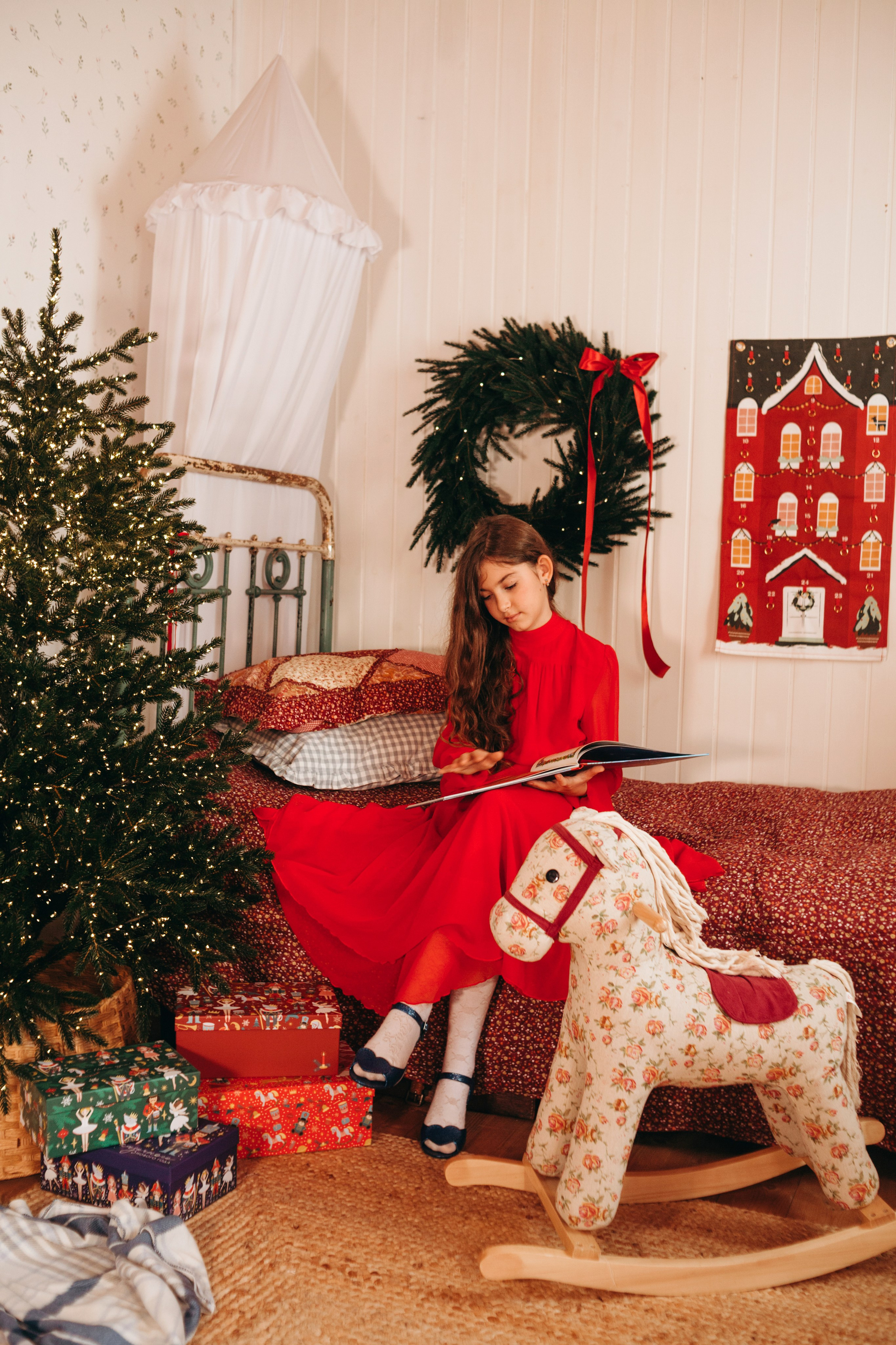 Девочка сидит рядом с украшенной новогодней елкой и праздничными игрушками.