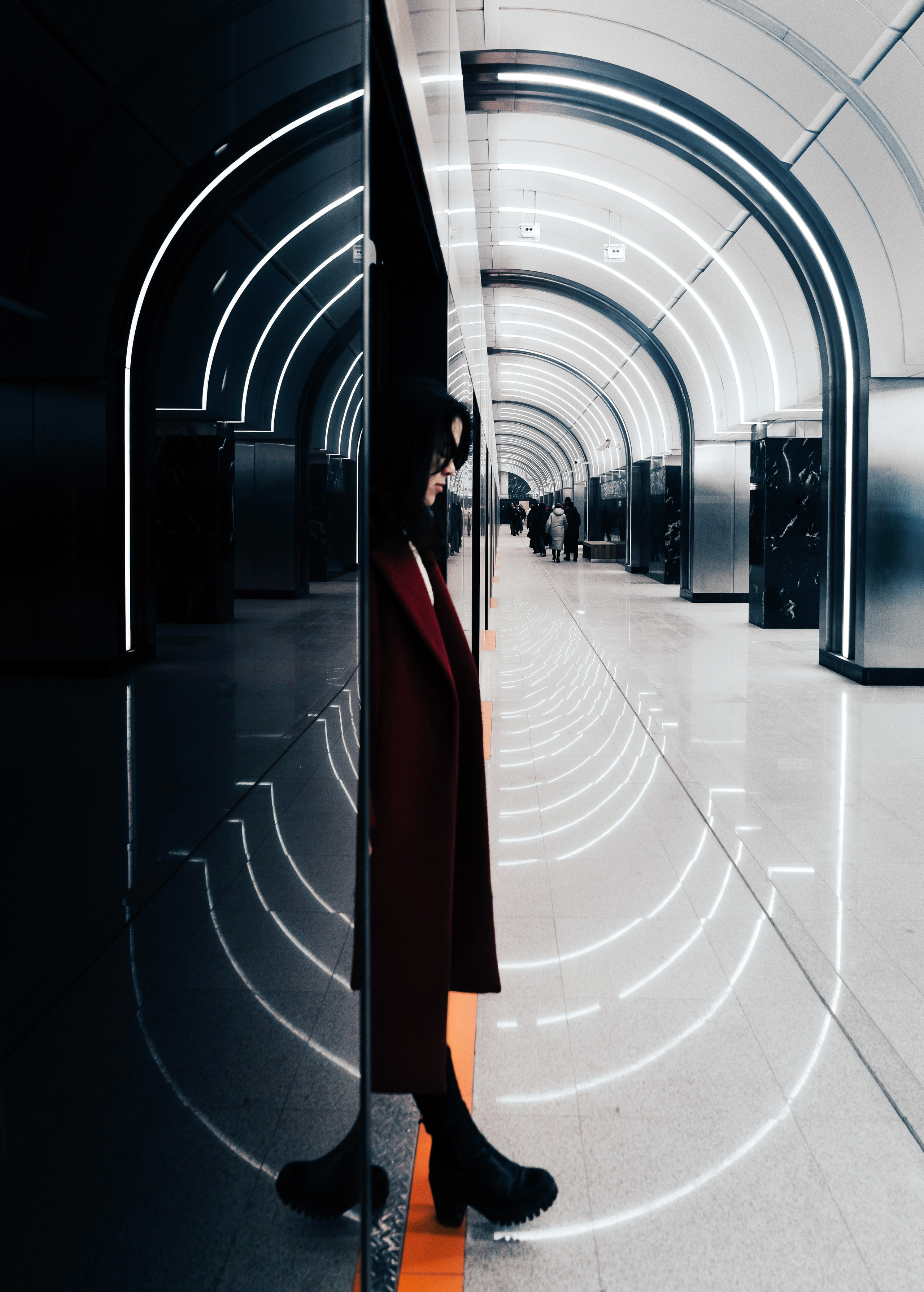 Метро СПБ Путиловская. Девушка в красном пальто в современном вестибюле станции метро Санкт-Петербурга, отражение в зеркальной колонне, урбан-портрет, фотограф Мальцев Евгений.