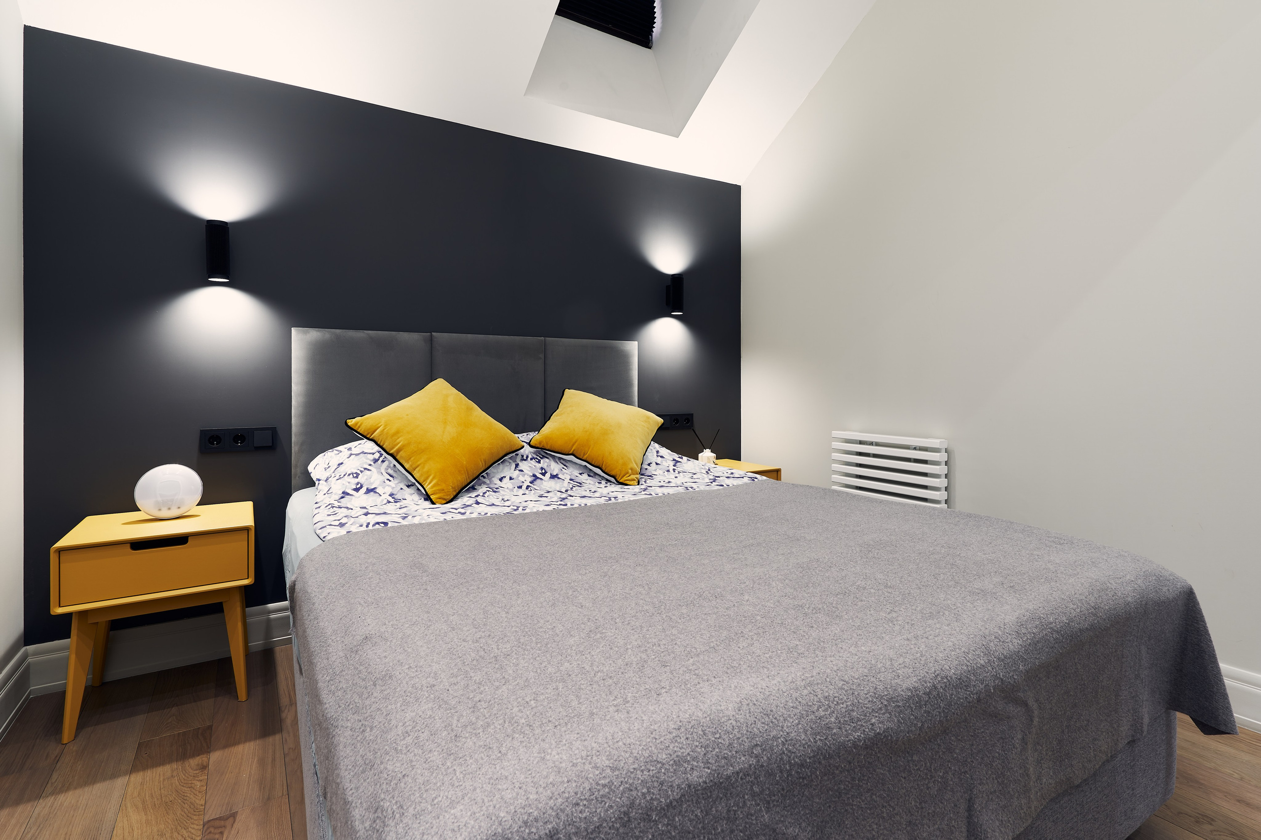 Интерьерная фотография спальни в уютных московских апартаментах с кроватью на фоне черной стены с включенными ночниками