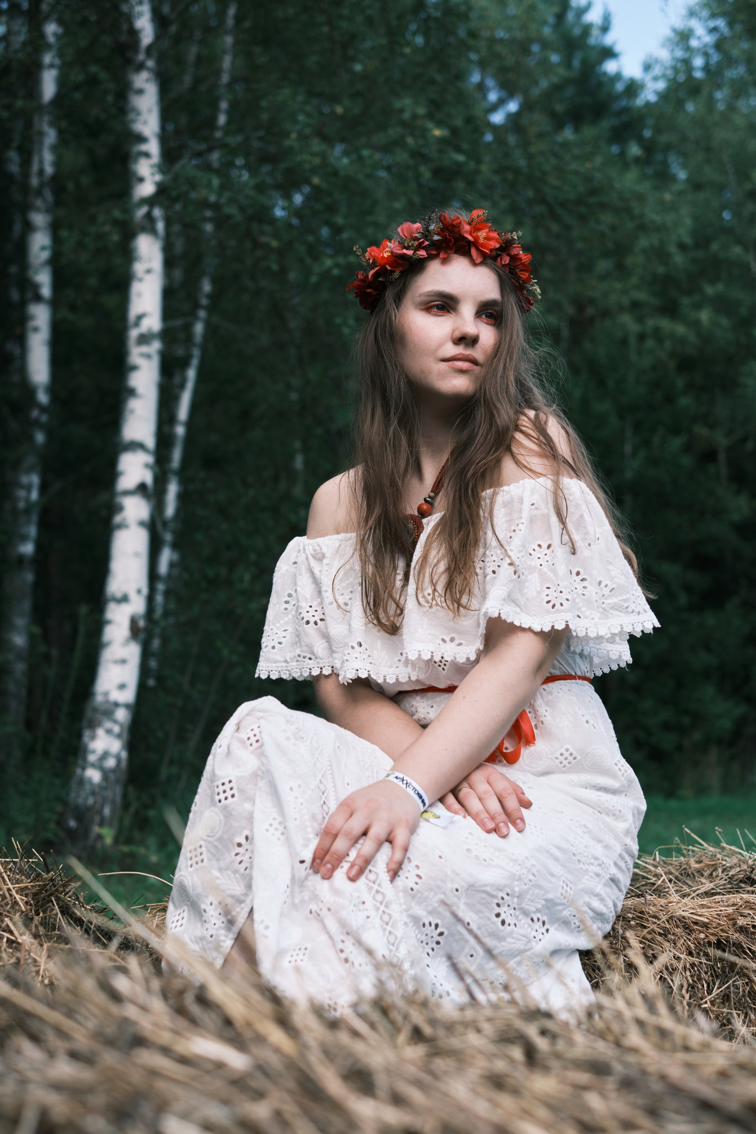 Девушка в белом сарафане и венком на голове сидит на сене