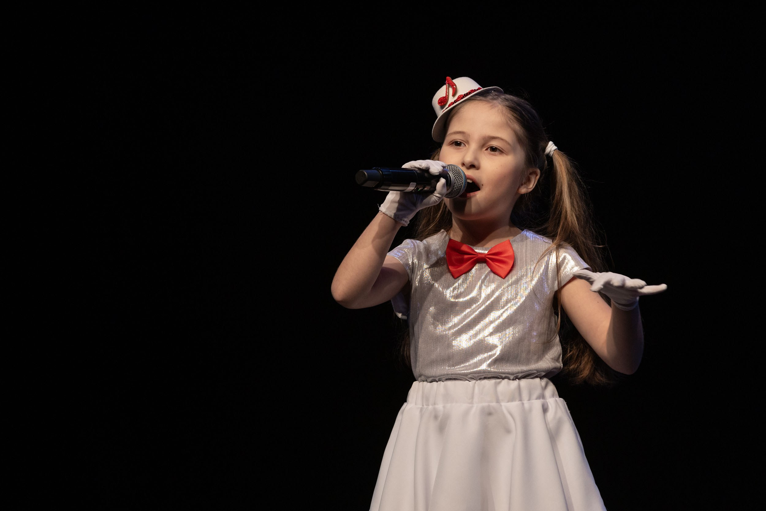 Девочка 7-8 лет поет в микрофон на черном фоне.