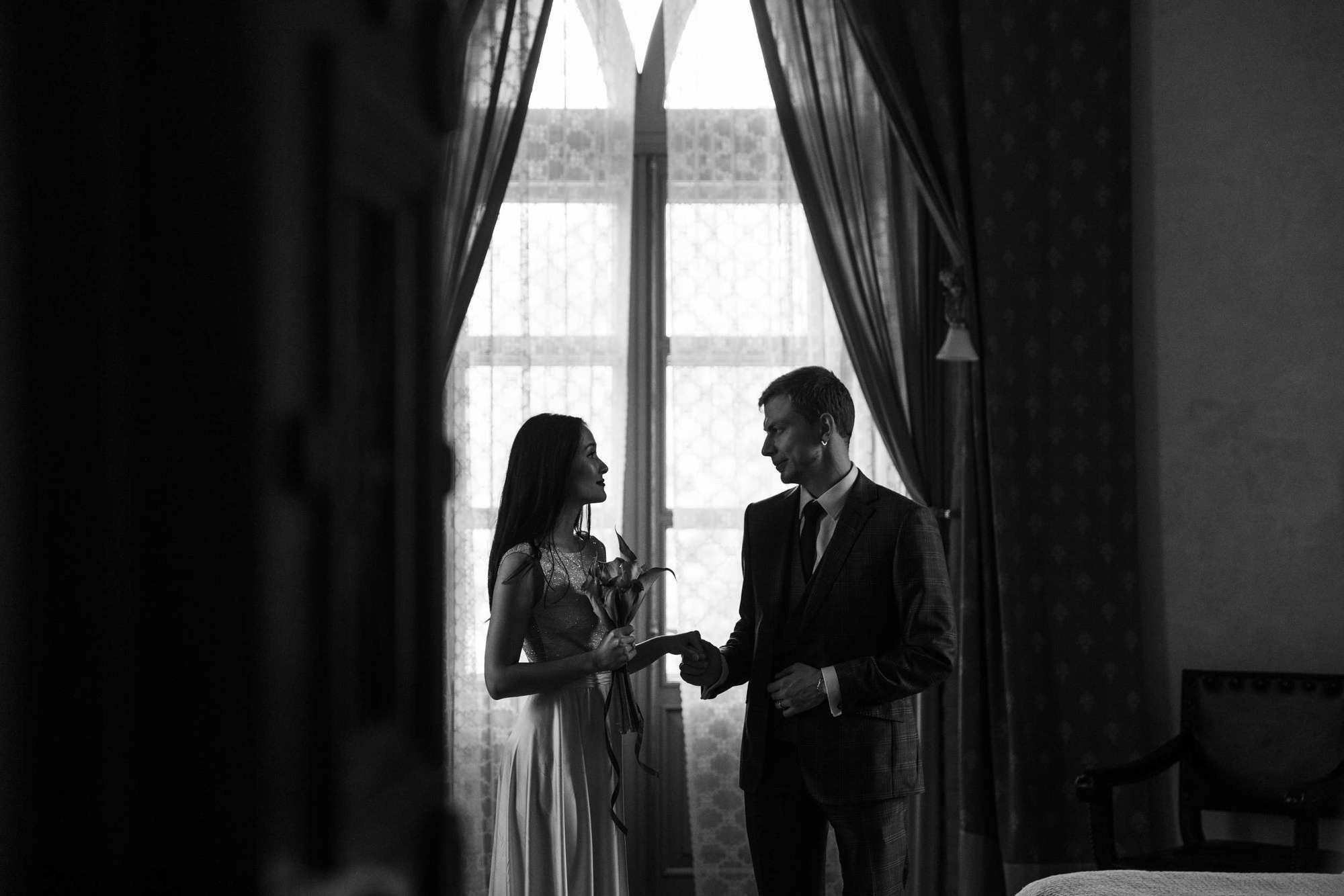 Невеста и жених стоят напротив окна
