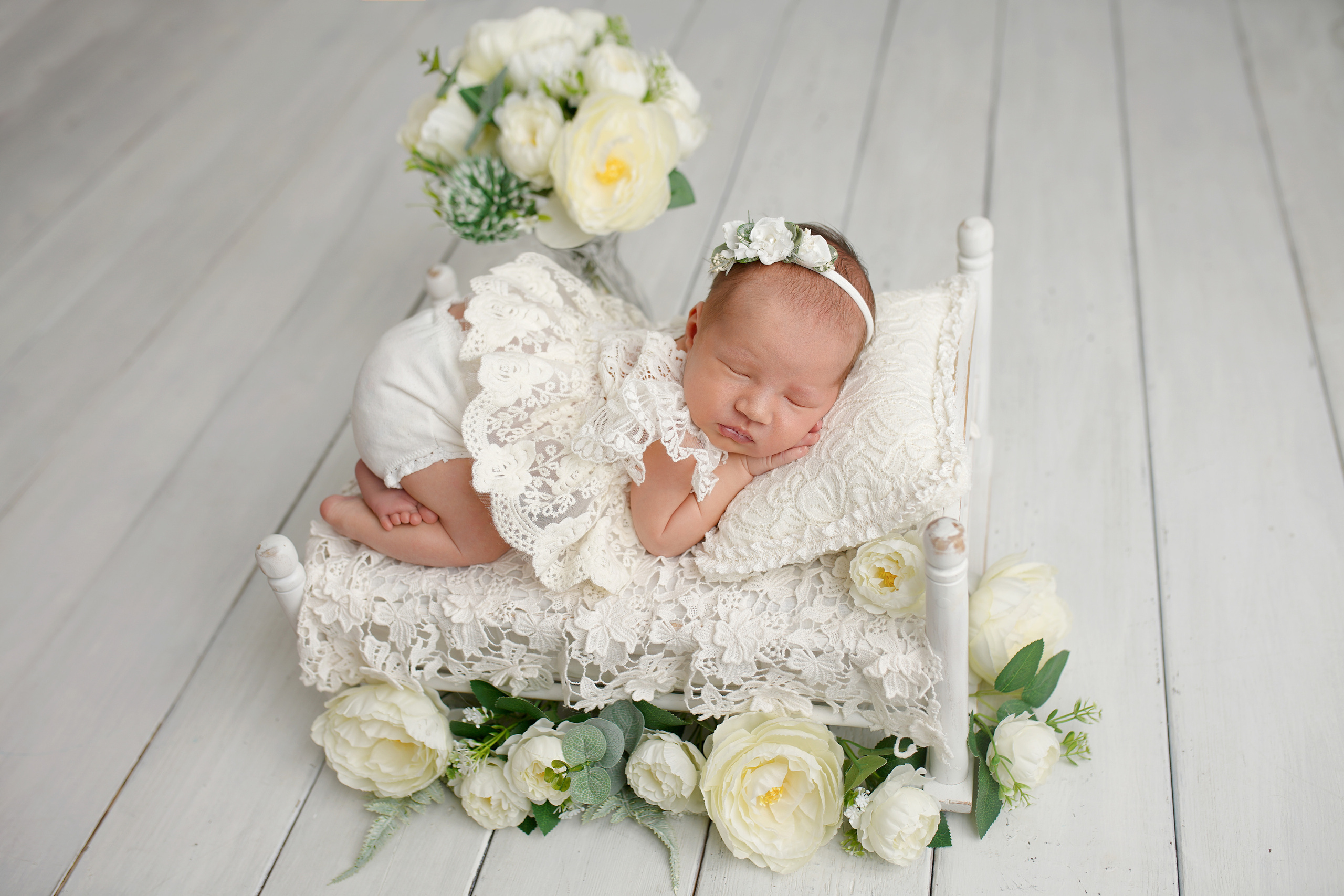 Детский  фотограф красиво уложил новорожденную девочку на кроватку и сфотографировал.