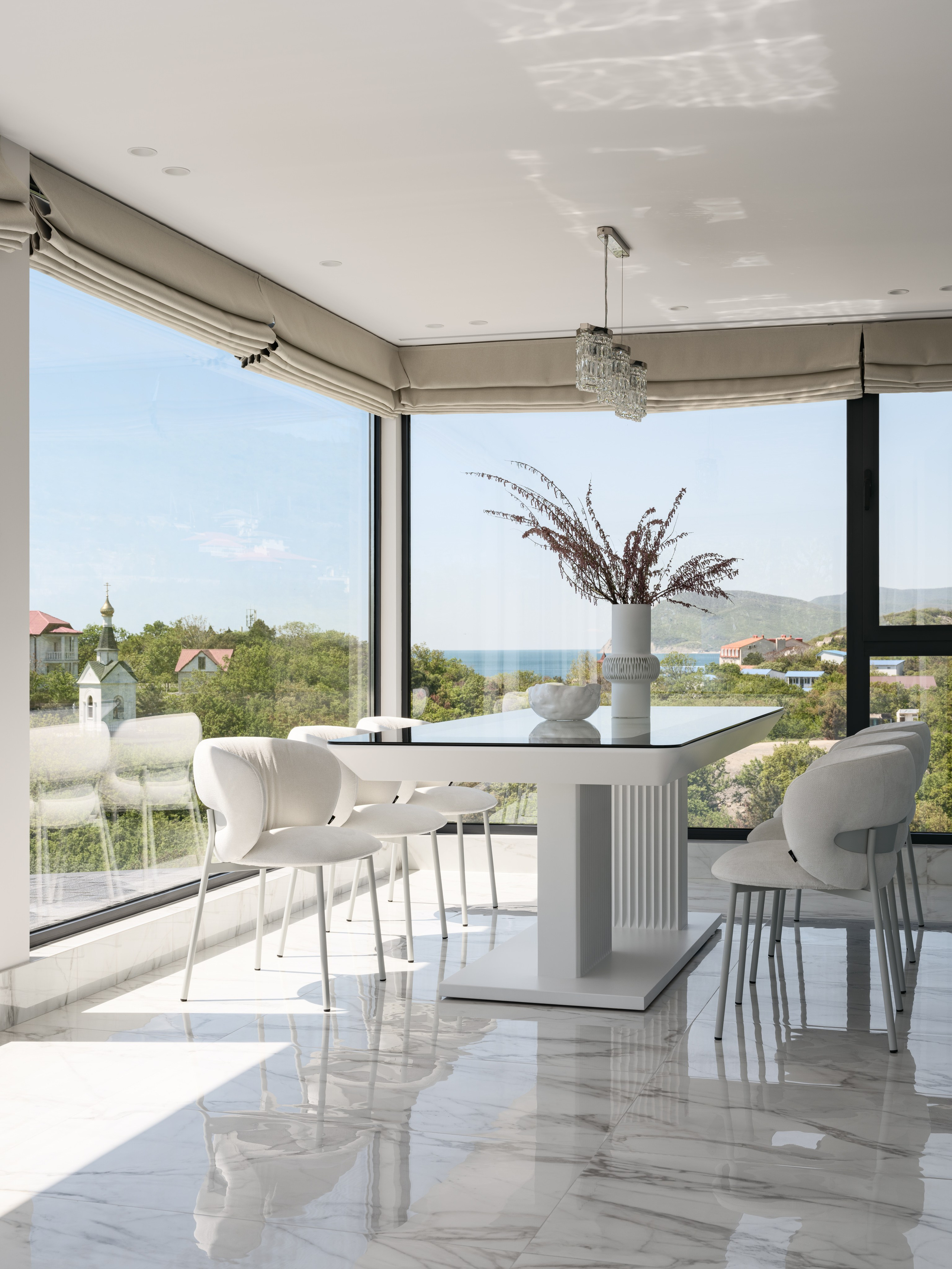 Современная столовая с панорамными окнами и видом на зелёные холмы, интерьер в светлых тонах с мраморным полом и минималистичной мебелью. Дизайн разработан Алёной Боярской, стилизация Натальи Якушевой, фотосъёмка Сергея Денисенко.