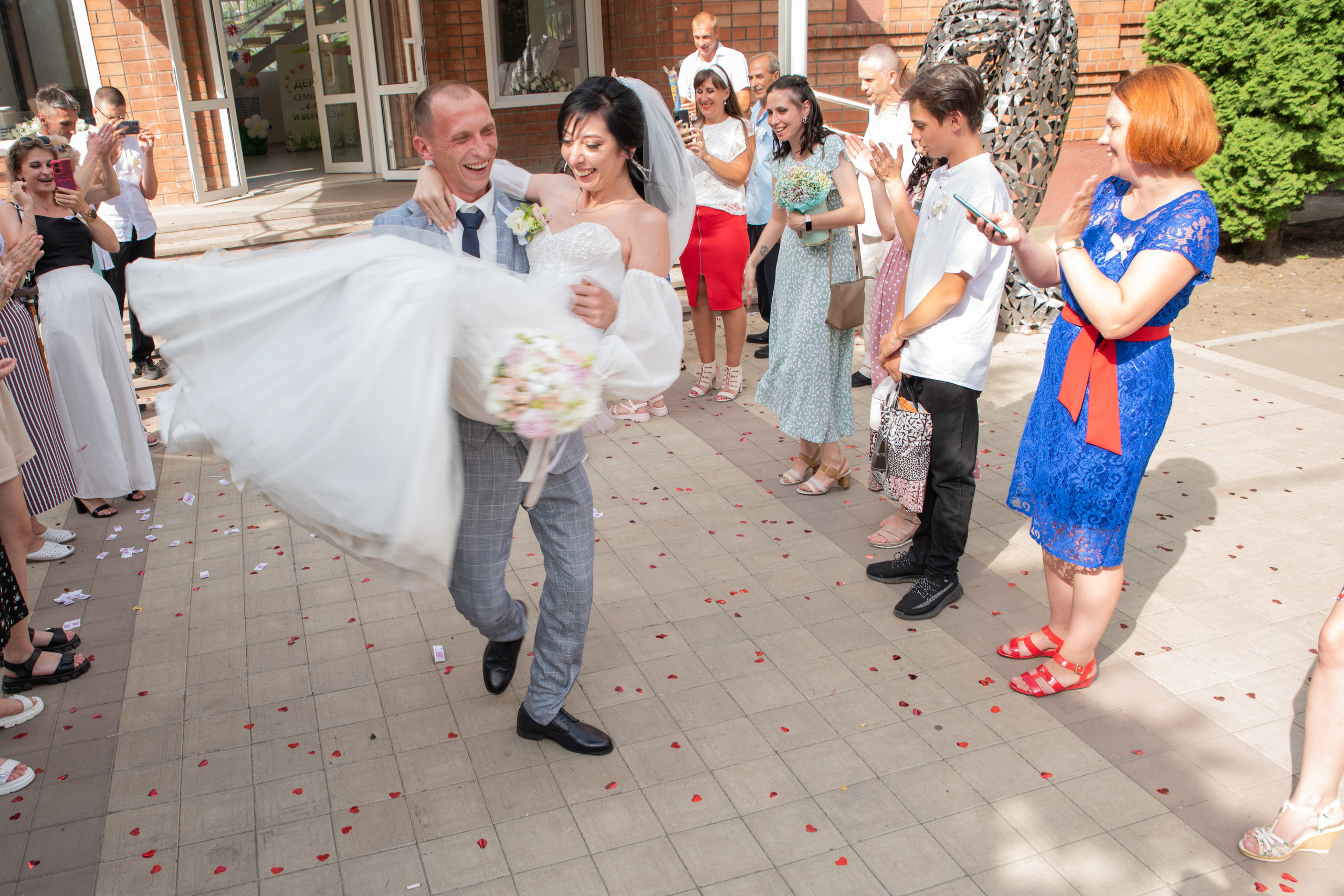жених выносит невесту на руках из загса им аплодируют гости