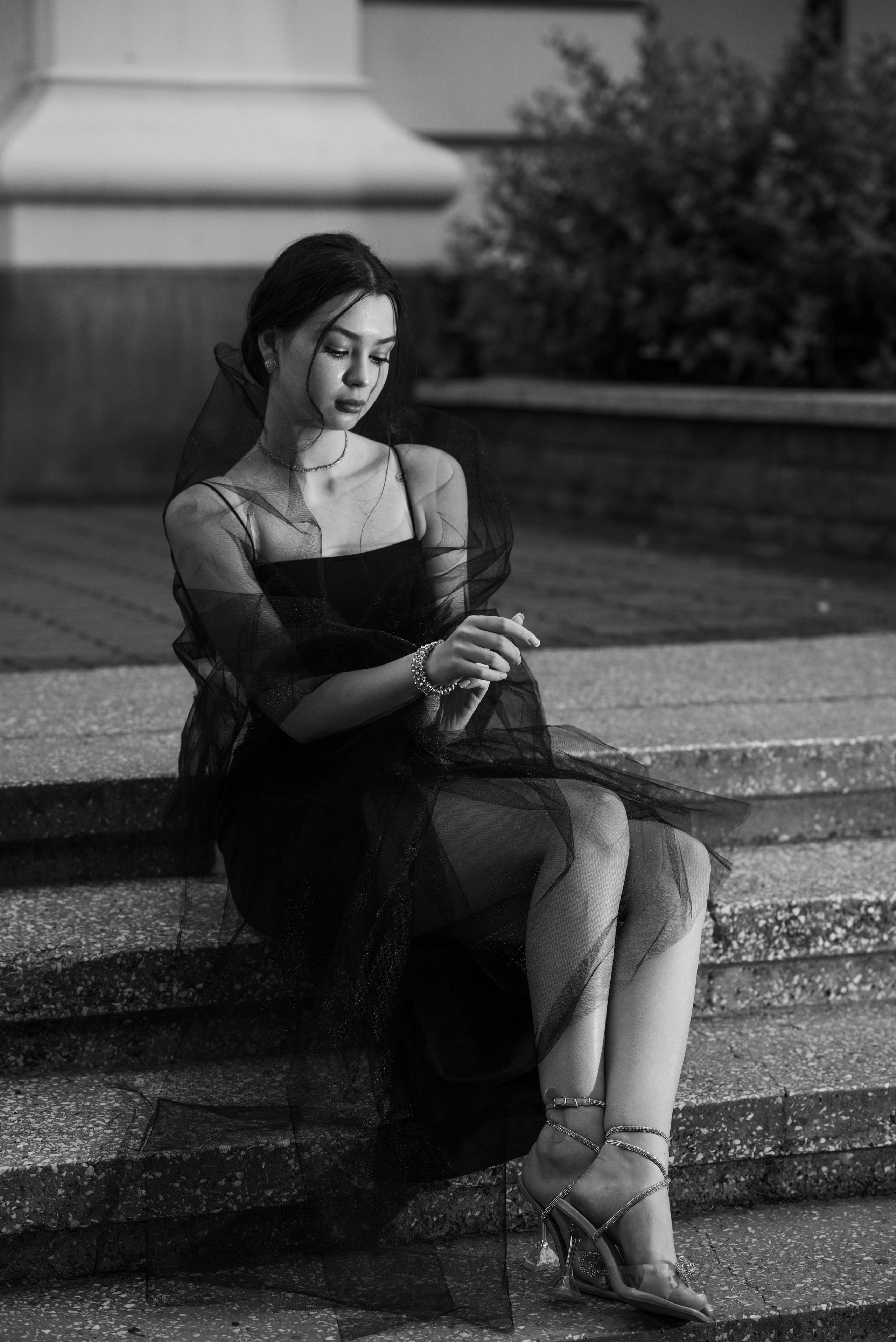 девушка сидит вечером на ступеньках в парке в черном вечернем платье и с черной фатой
