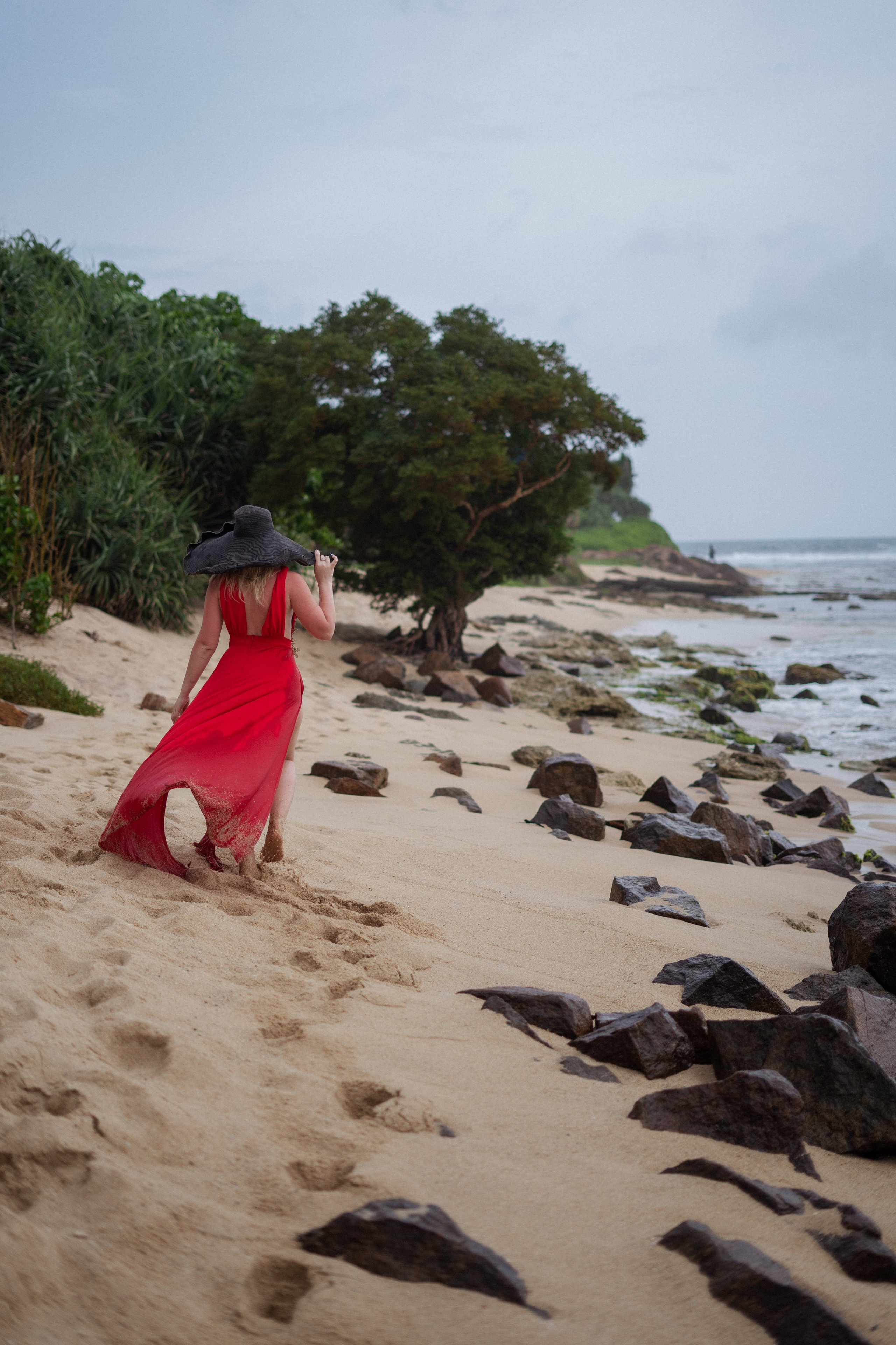 a beautiful blonde in a red dress smiling on the shore of the ocean