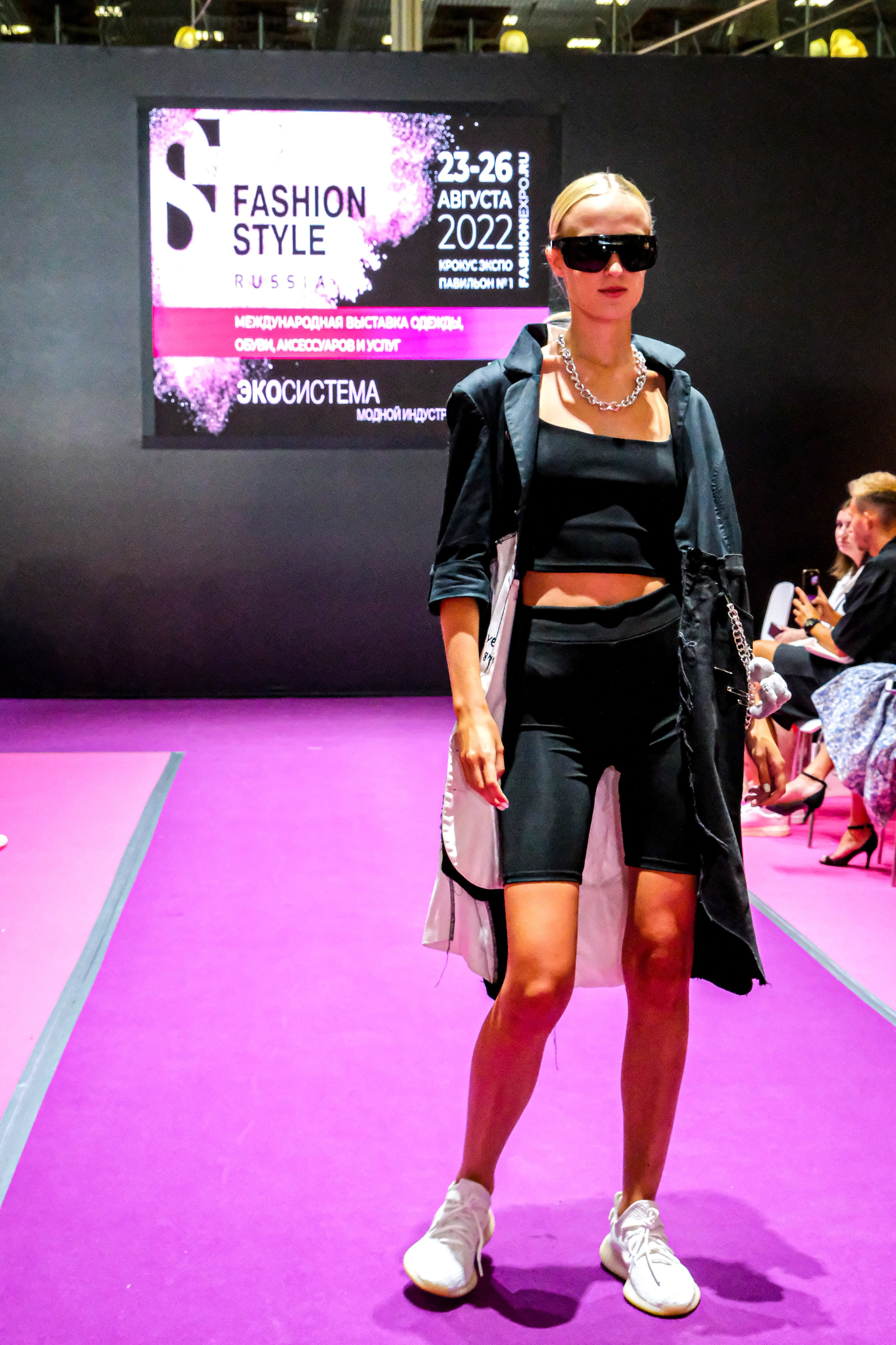  "Модели в ярких нарядах проходят по подиуму во время показа мод, освещенные яркими софитами и окруженные восторженными зрителями."