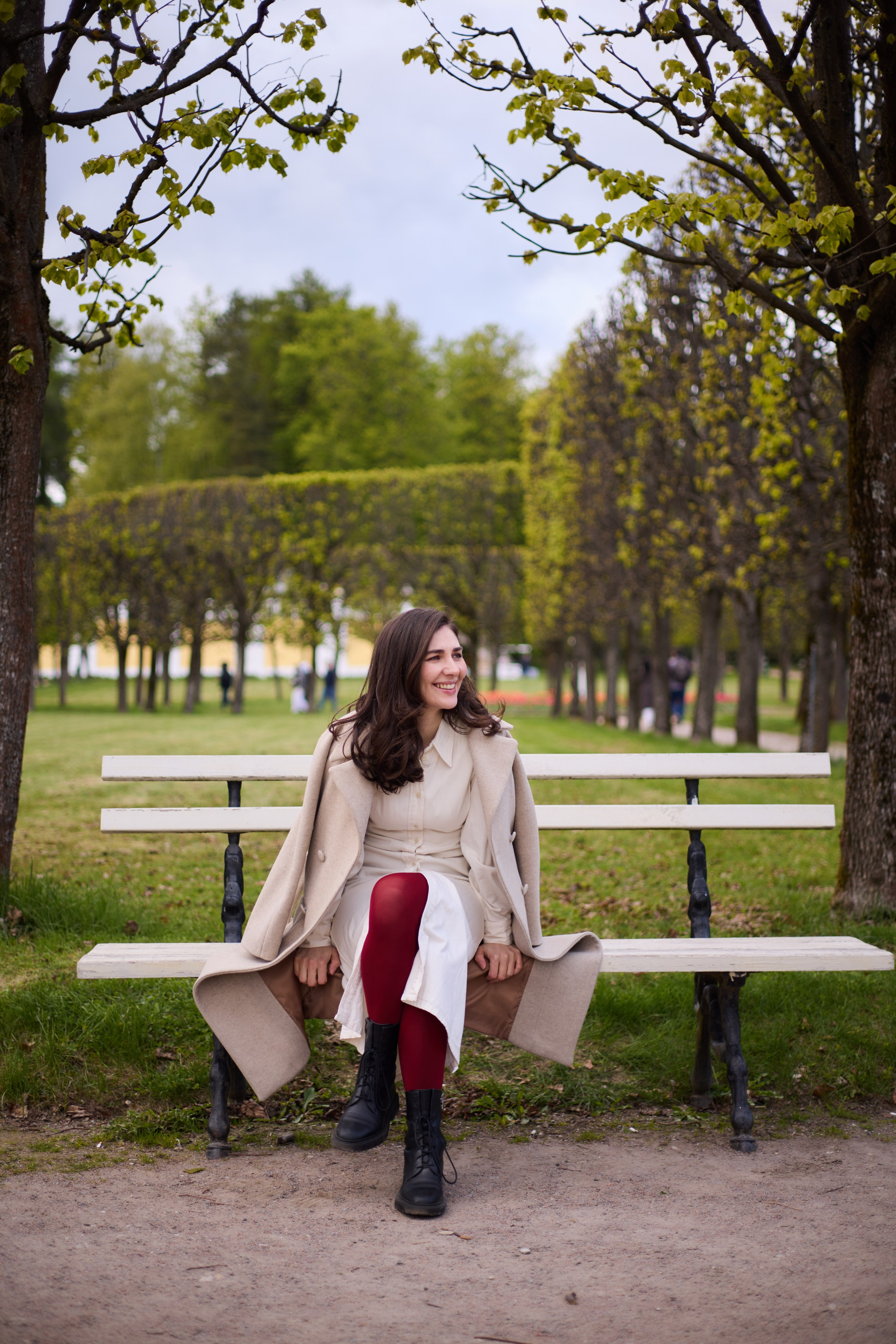 Фотосессия в Архангельском с Астой Габлия в белом платье и бежевом пальто, с красными колготками сидящей на скамейки